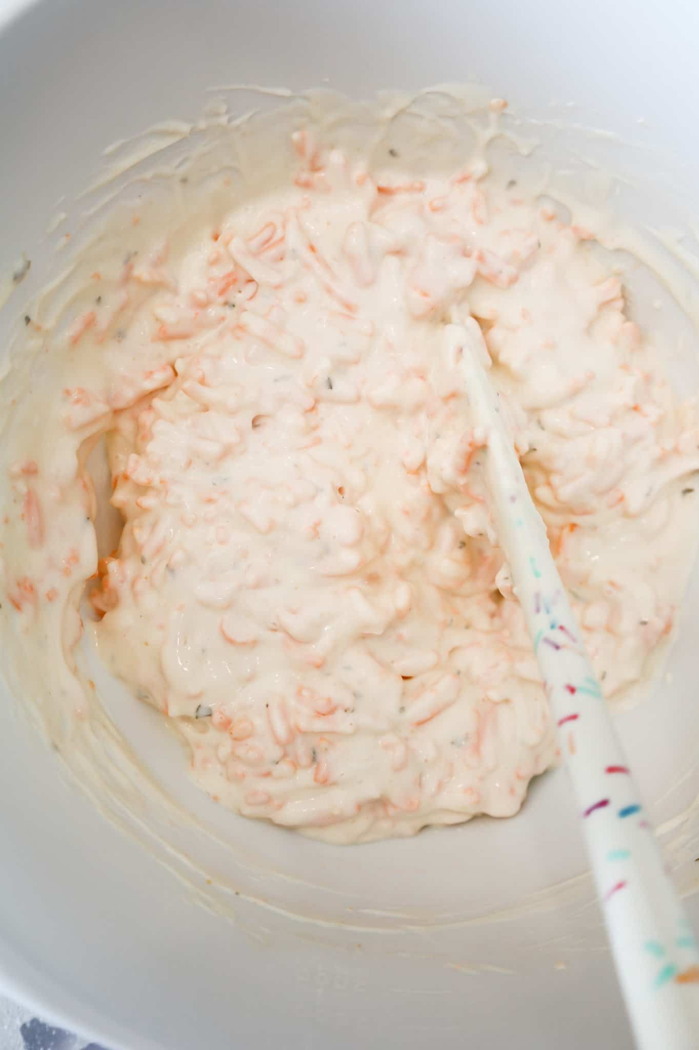 shredded cheddar, mayo and ranch dressing mixture being stirred in a mixing bowl