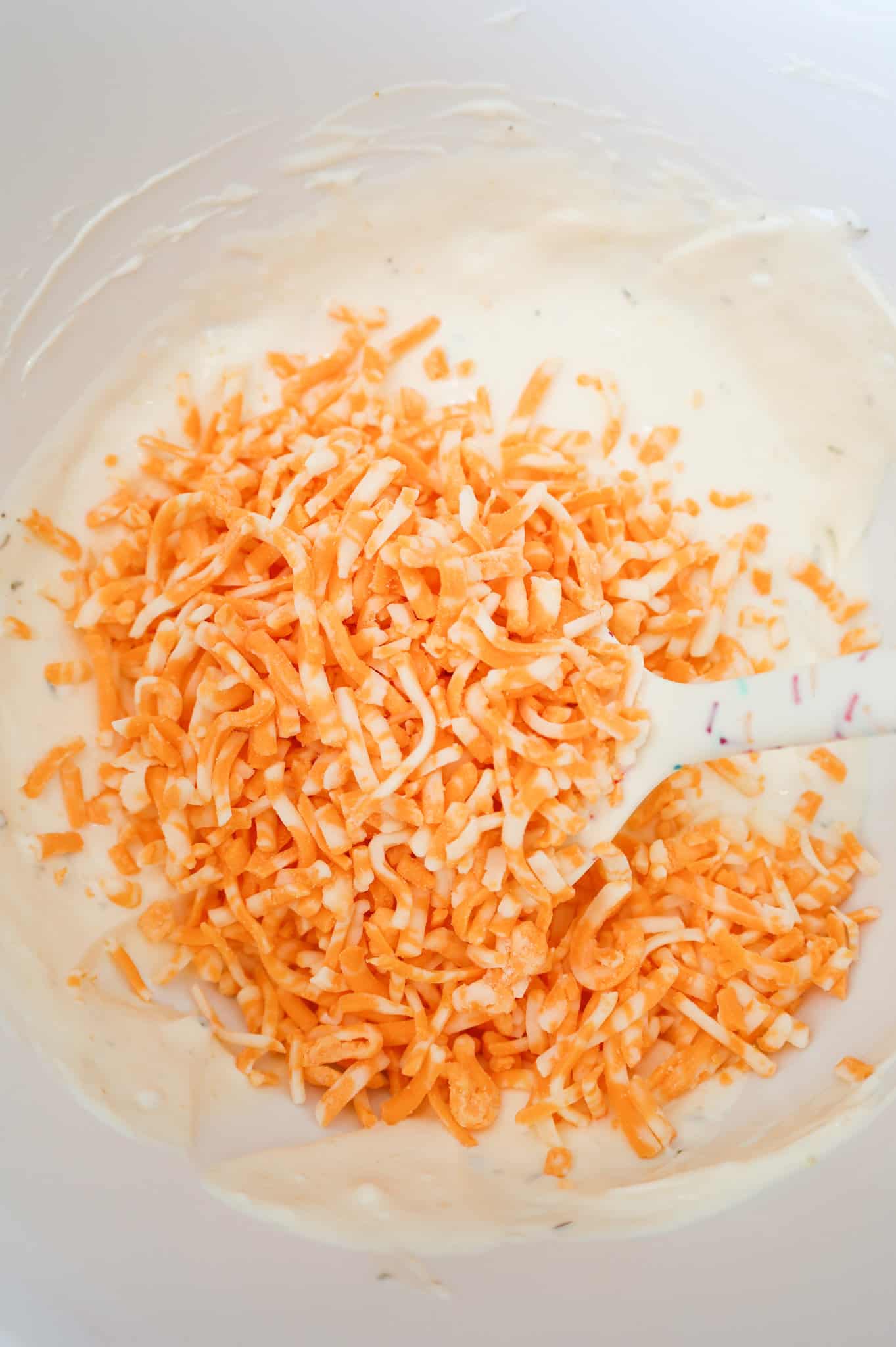 shredded cheddar on top of mayo and ranch dressing in a bowl