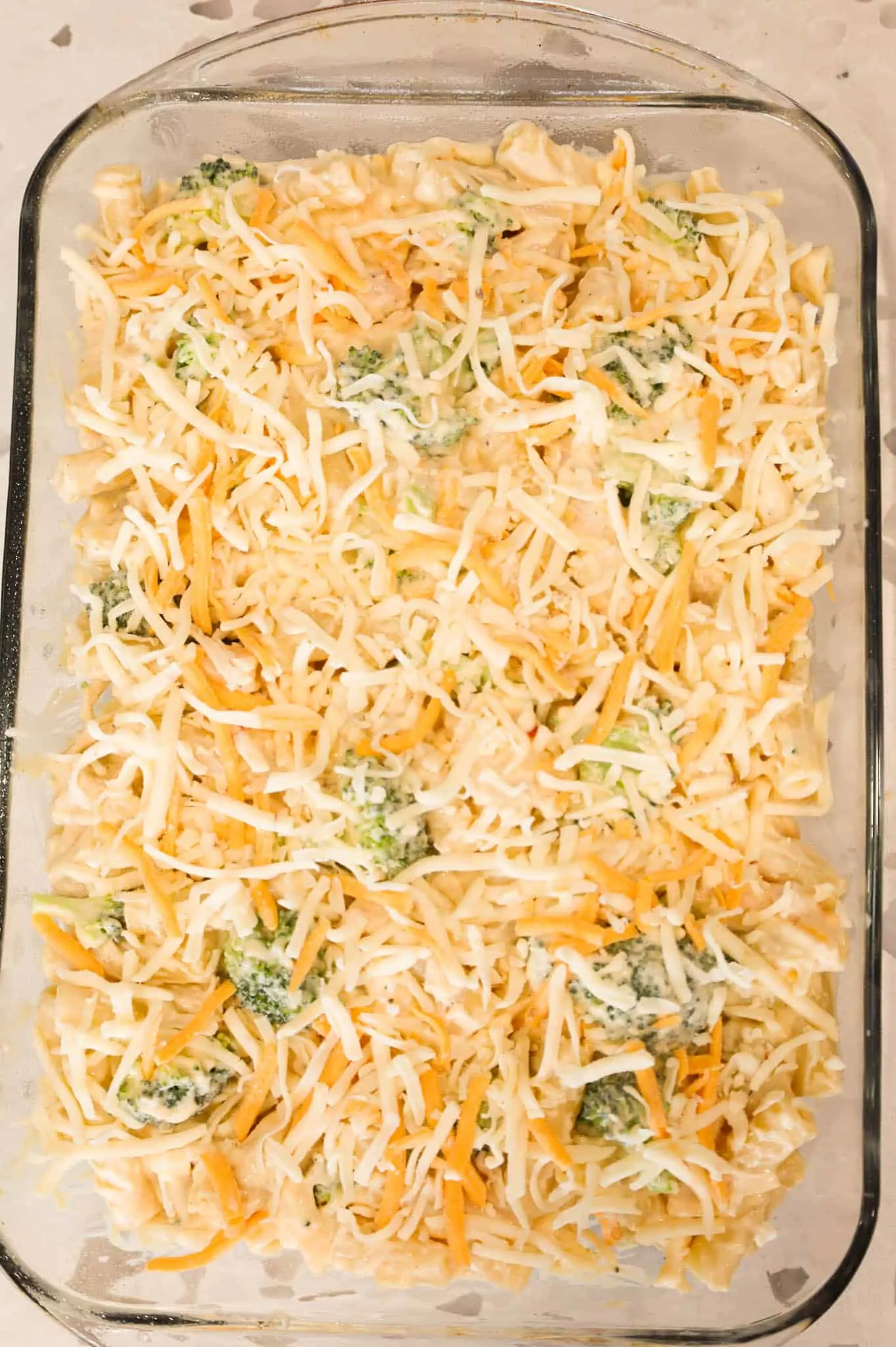 shredded cheese on top of creamy chicken and broccoli ziti mixture in a baking dish
