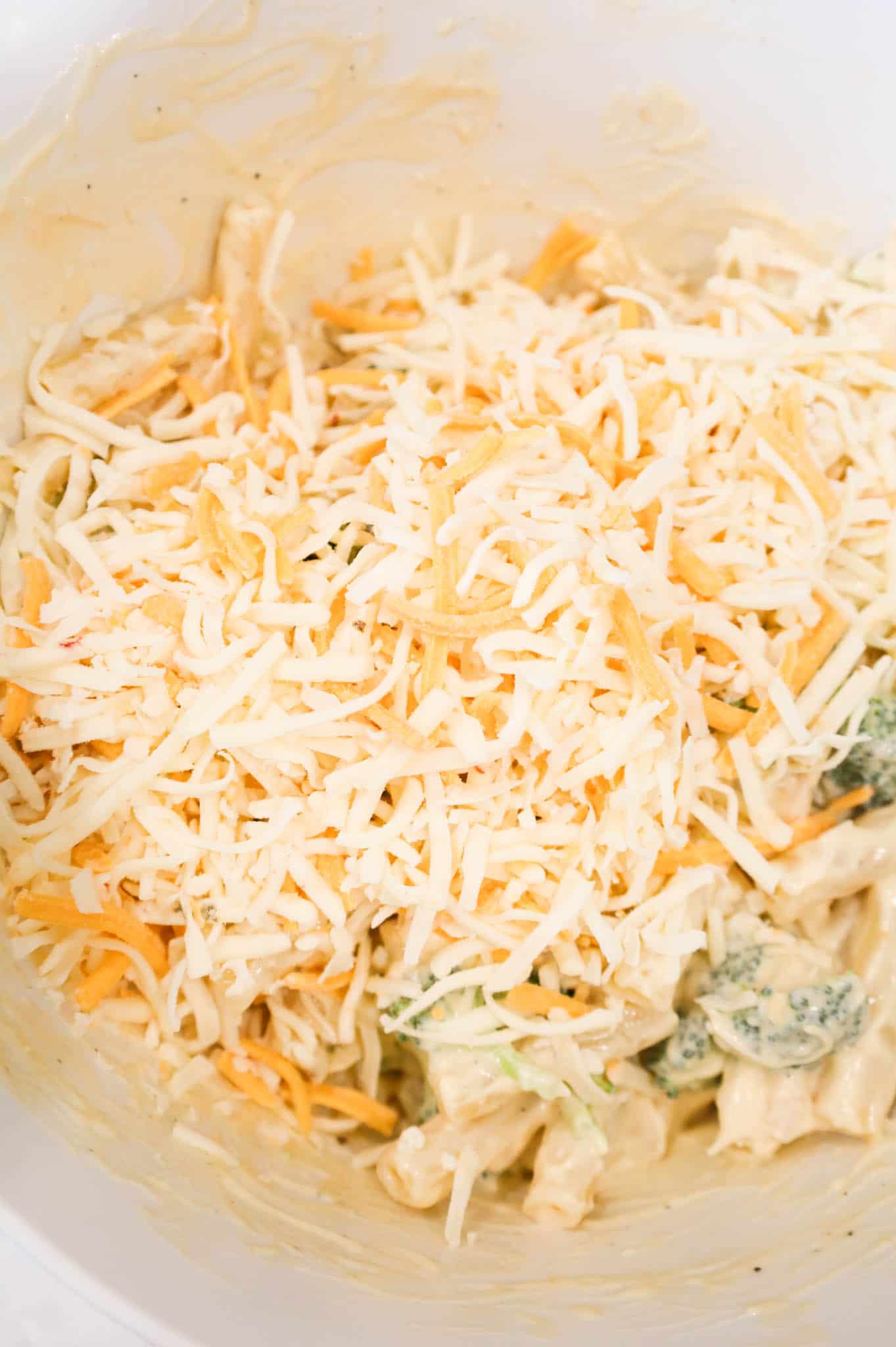 shredded cheese on top of creamy chicken and ziti mixture in a bowl