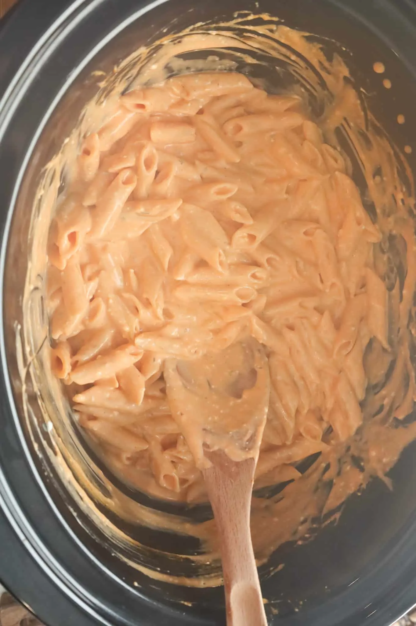 stirring penne noodles in Buffalo sauce in a crock pot