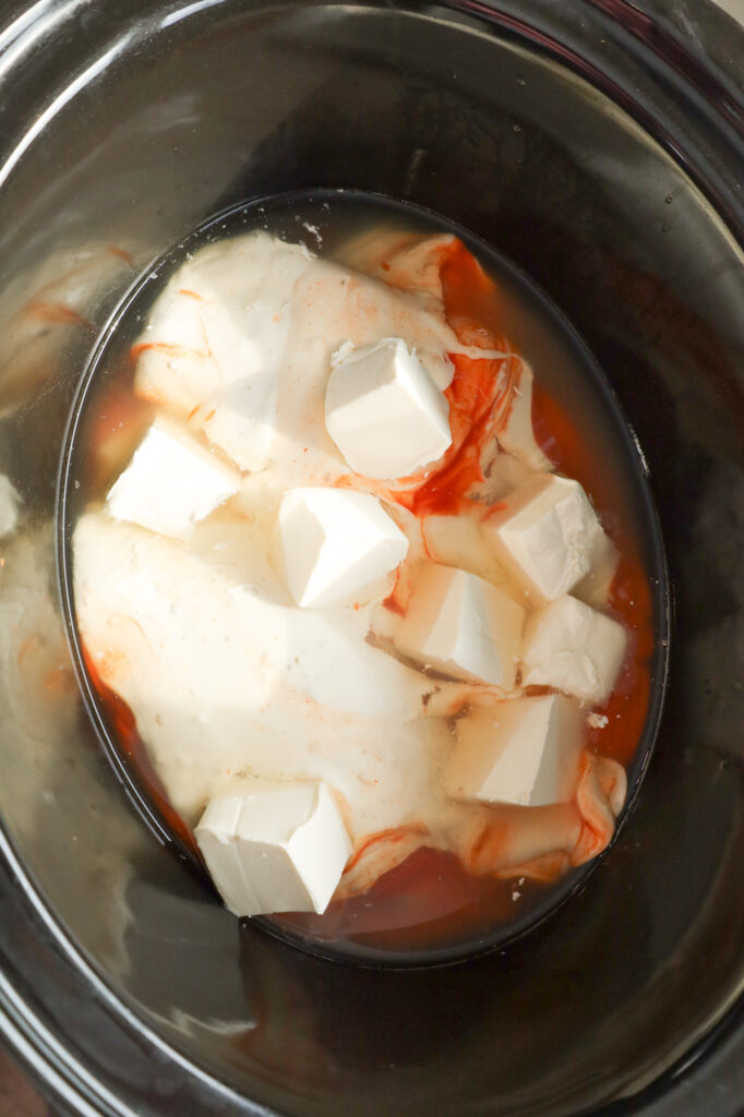 cream cheese cubes, Buffalo sauce, ranch dressing and chicken broth on top of chicken breasts in a Crock Pot