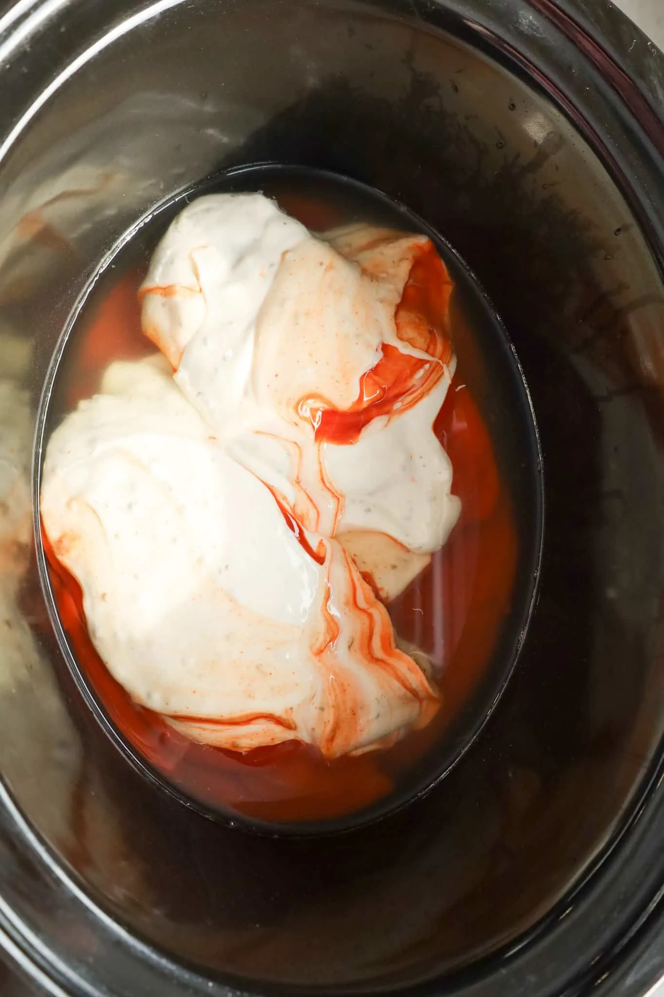 ranch dressing and Buffalo sauce on top of chicken breasts in a crock pot