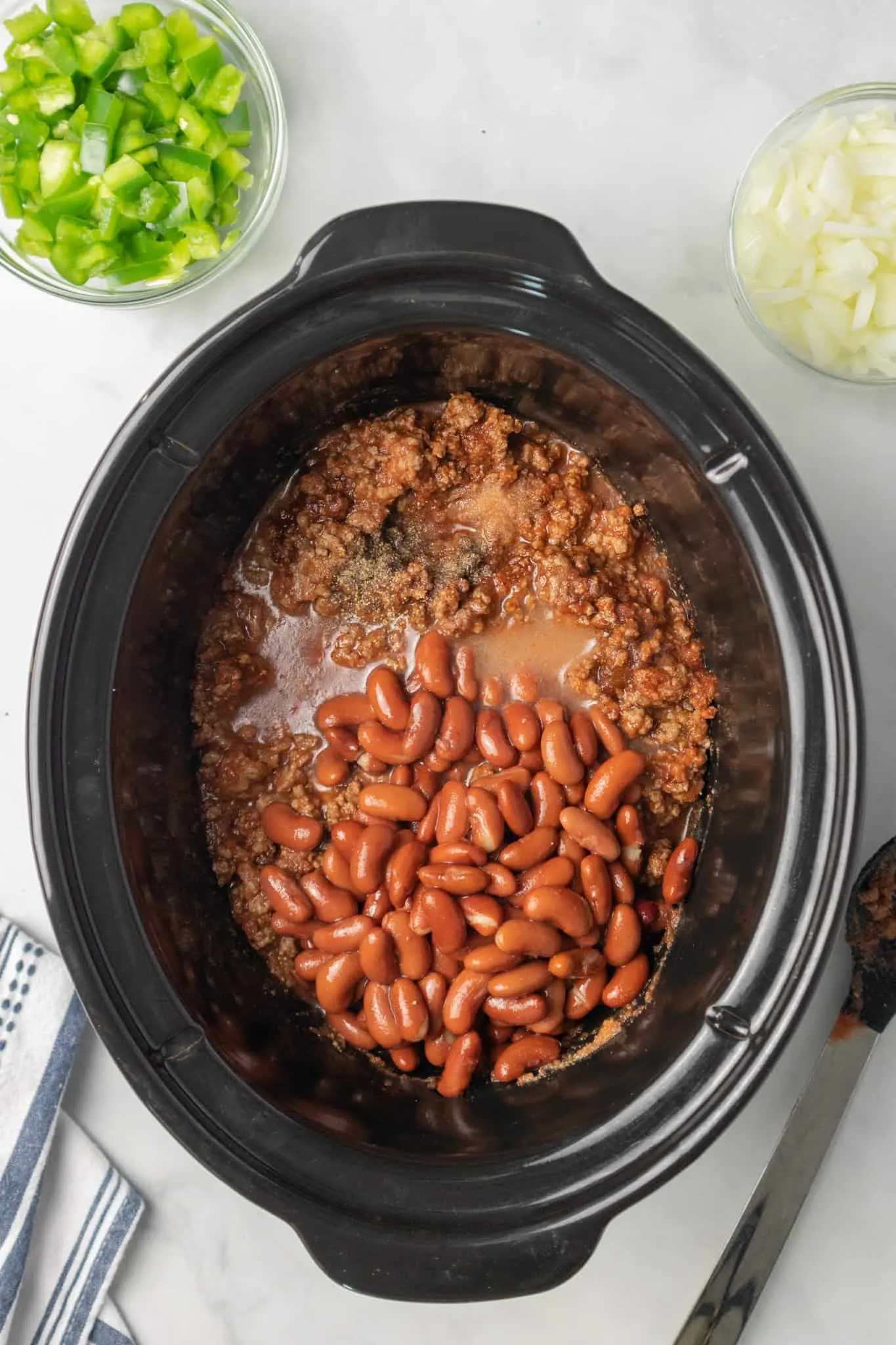 kidney beans on top of spices, ground beef and tomato sauce in a crock pot