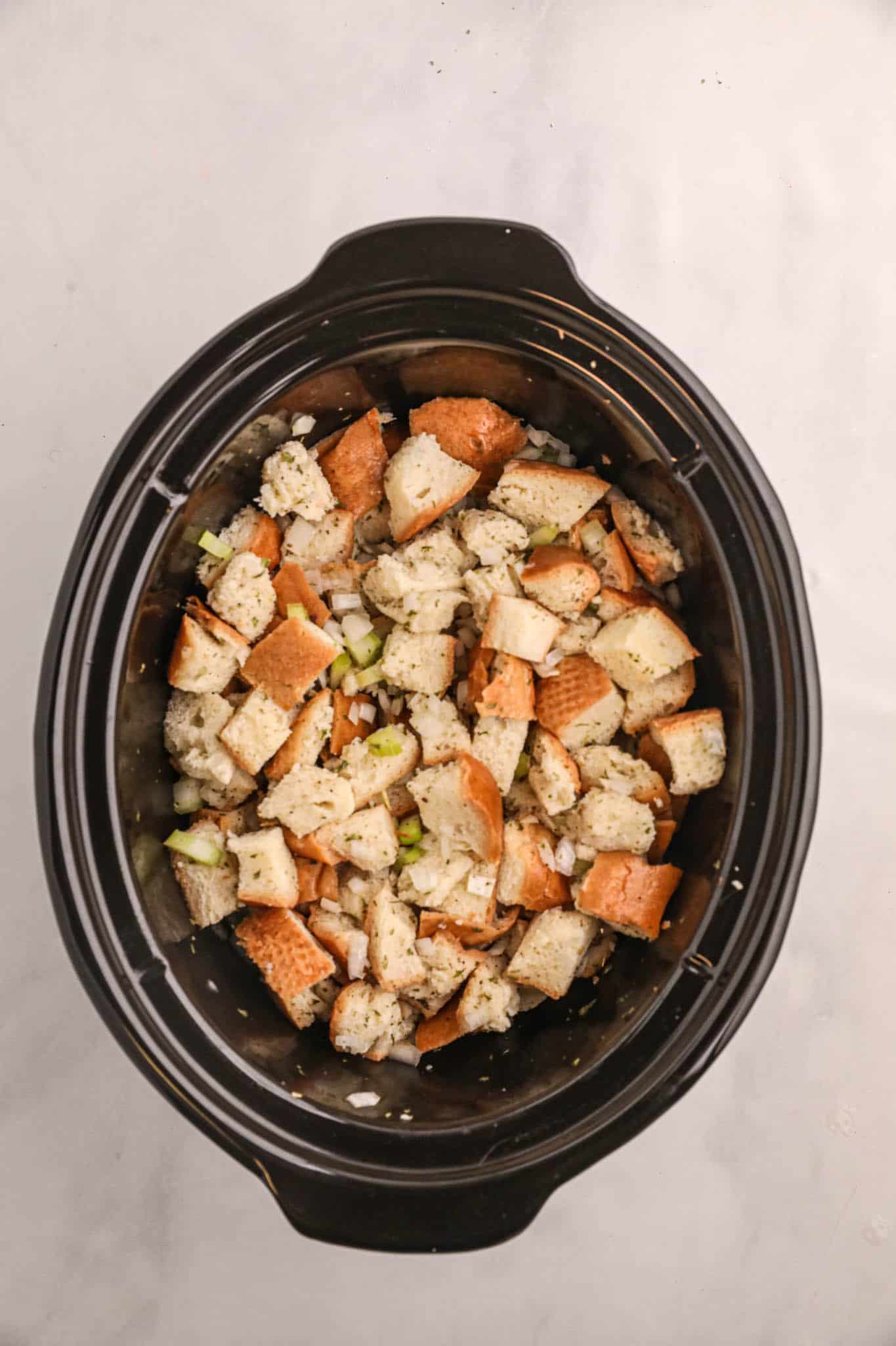 bread cubes stirred with melted butter and chopped veggies in a crock pot