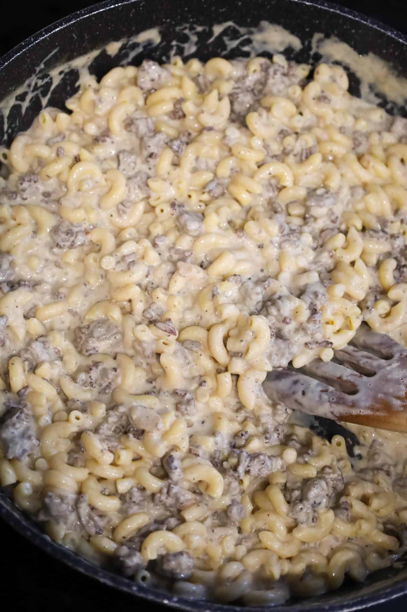 creamy ground beef macaroni being stirred in a skillet