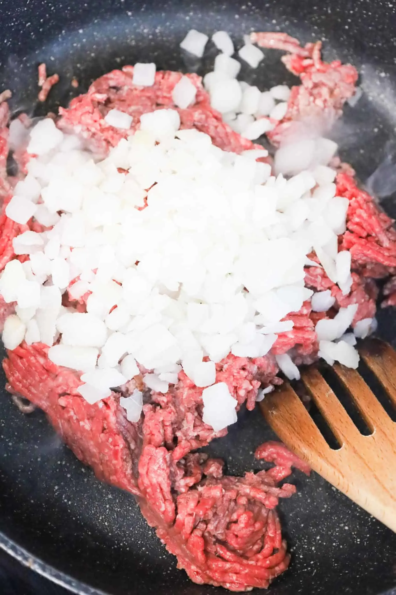 diced onions on top of ground beef in a skillet
