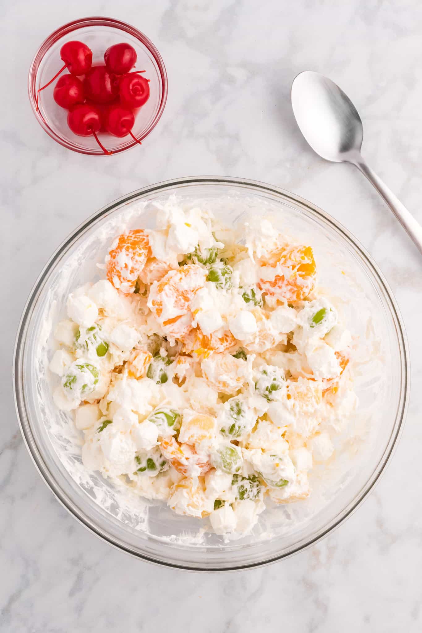 Cool whip and fruit salad ingredients being stirred together in a bowl