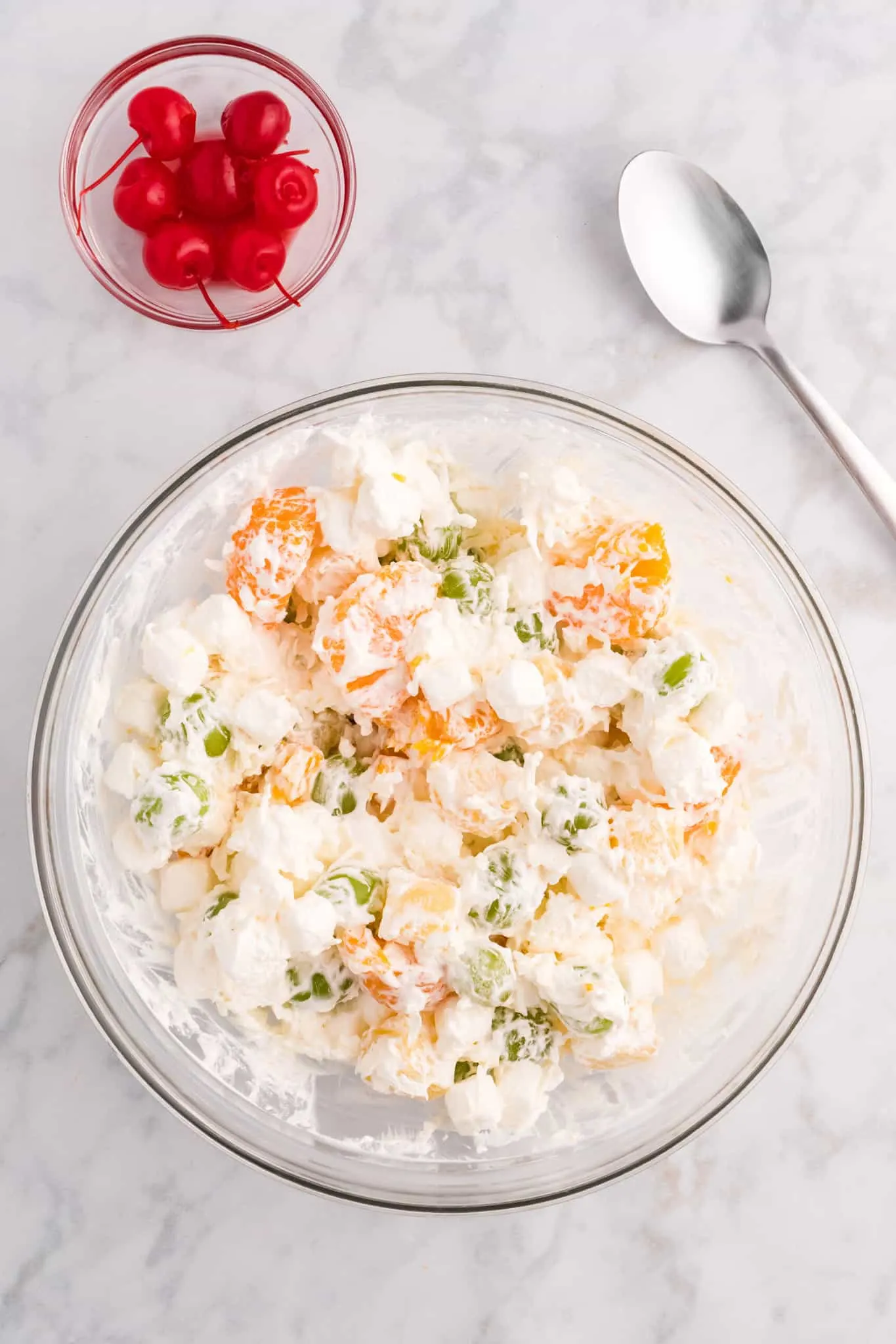 Cool whip and fruit salad ingredients being stirred together in a bowl