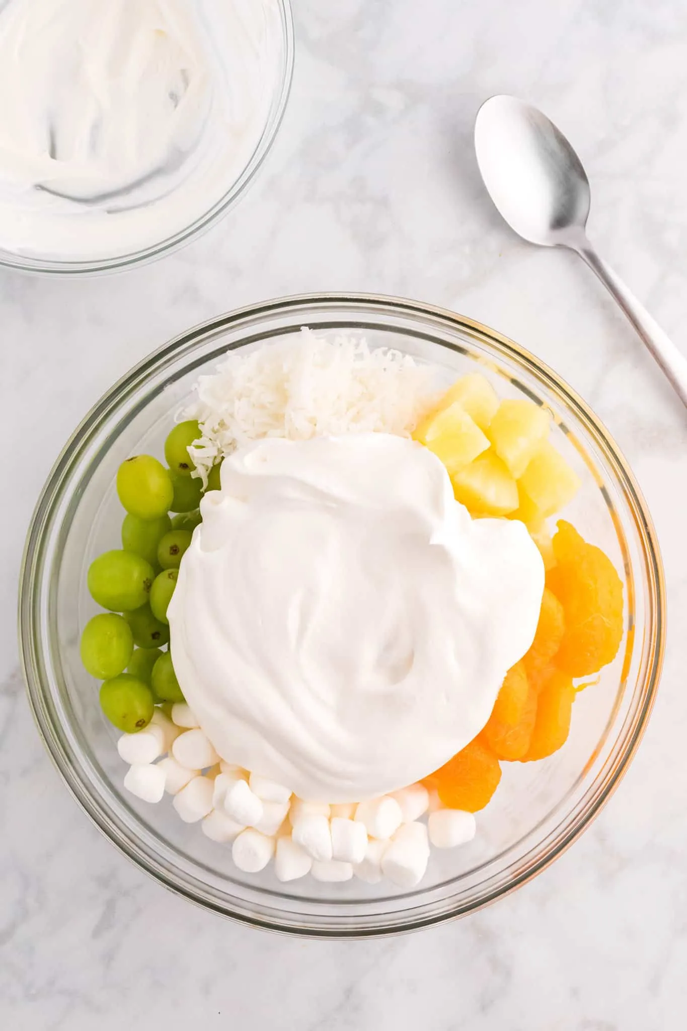Cool Whip on top of fruit salad ingredients in a bowl