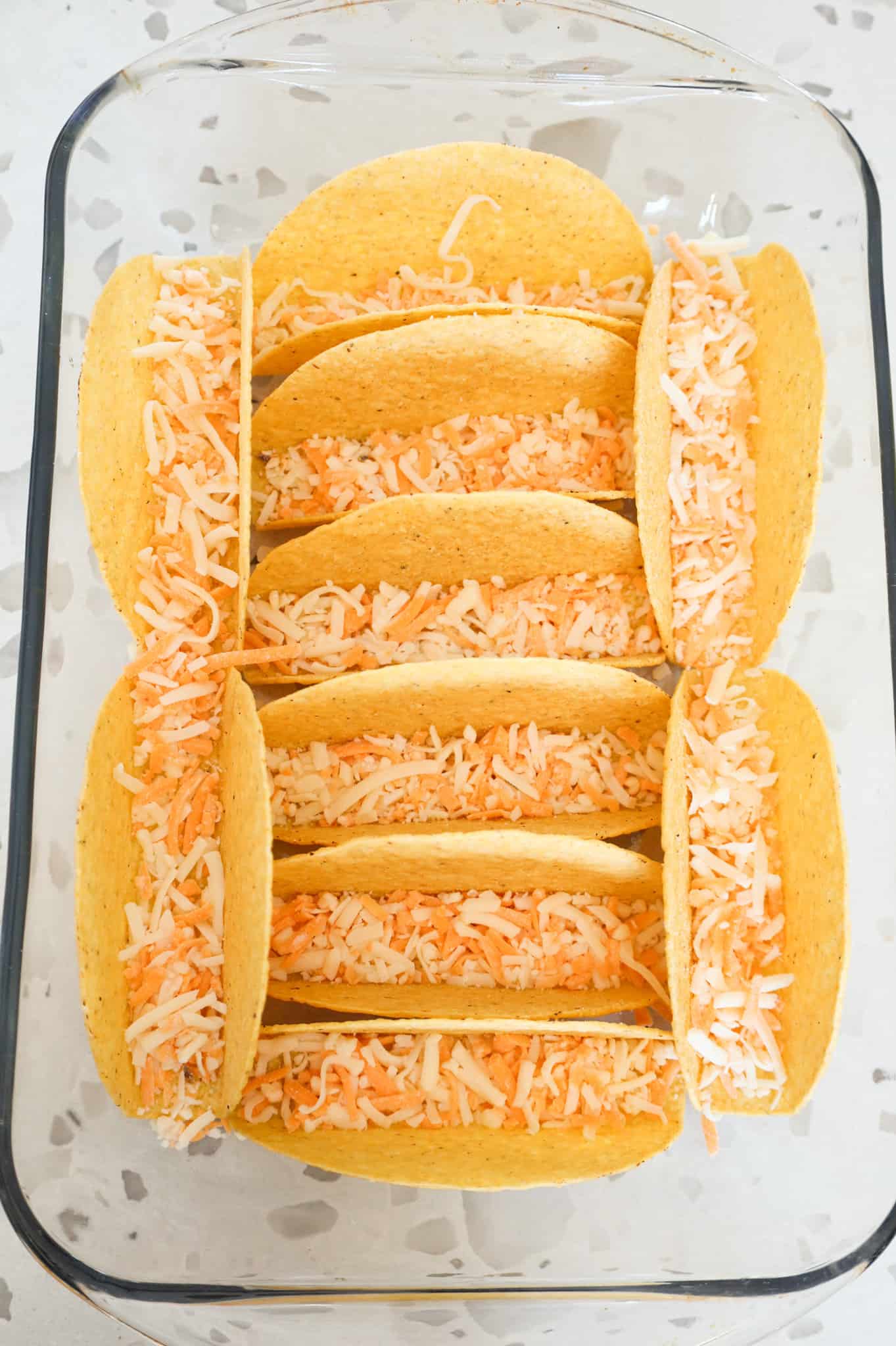 shredded cheese in the bottom of taco shells in a baking dish