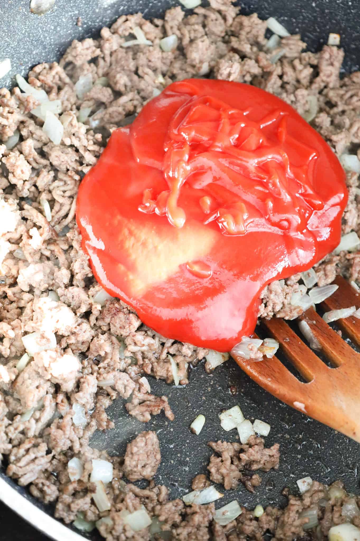 ketchup on top of cooked ground beef and diced onions in a skillet