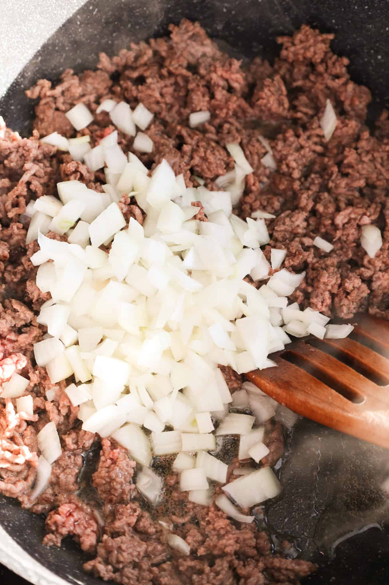 diced onions on top of ground beef in a skillet