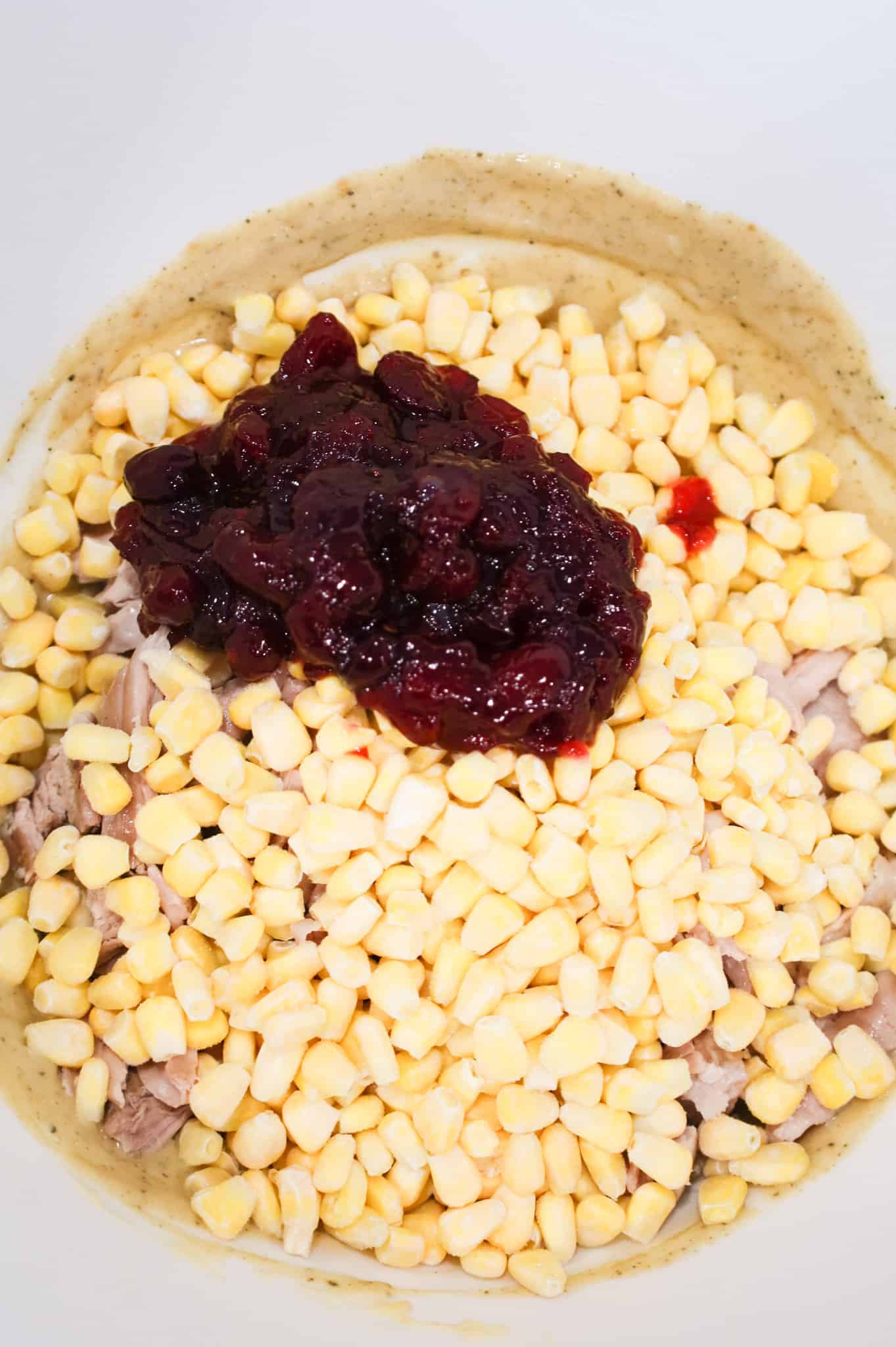 whole cranberry sauce on top of frozen corn, shredded turkey and cream of chicken soup mixture in a mixing bowl
