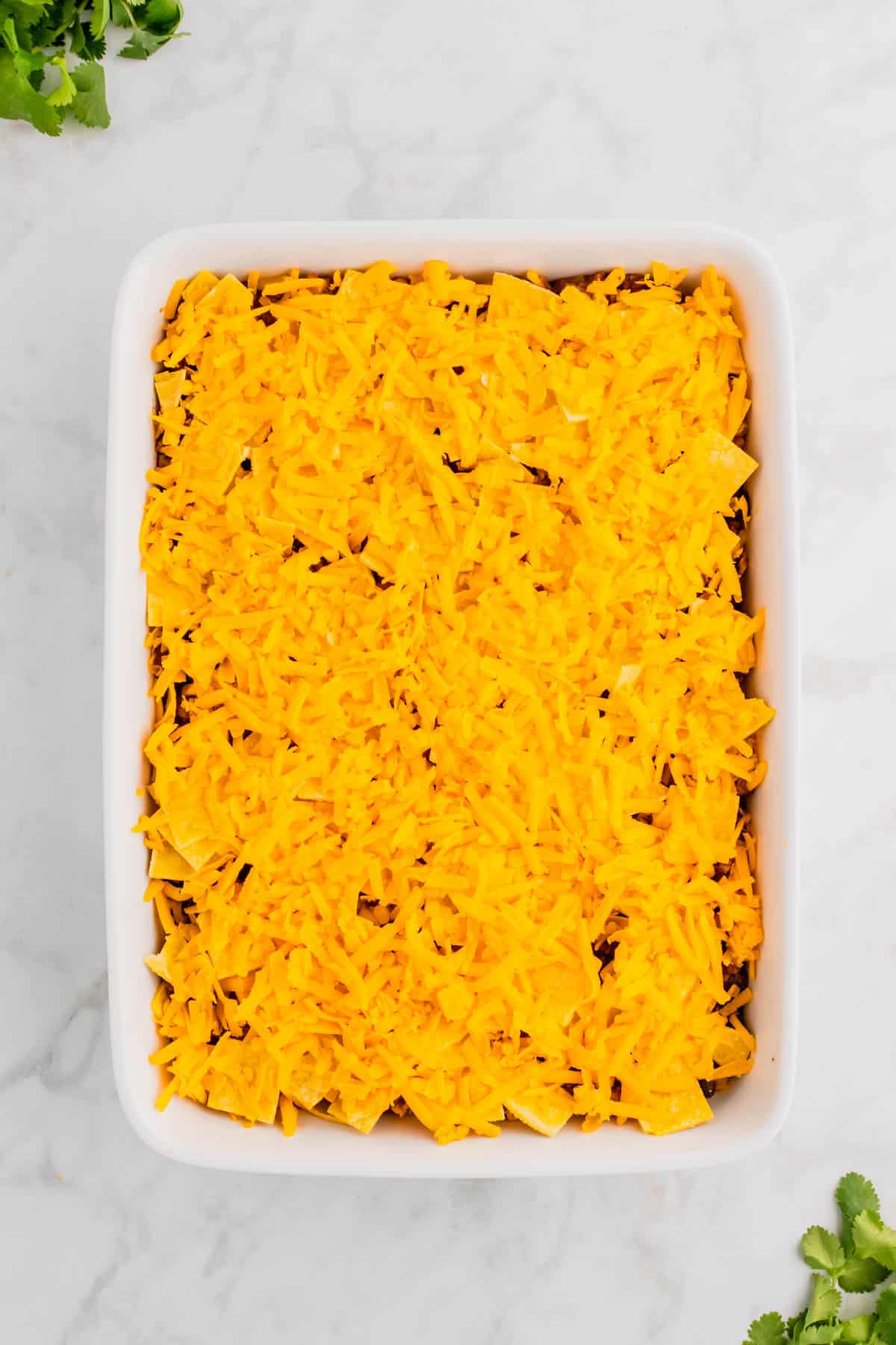 shredded cheddar and corn tortilla pieces on top of beef enchilada casserole in a baking dish