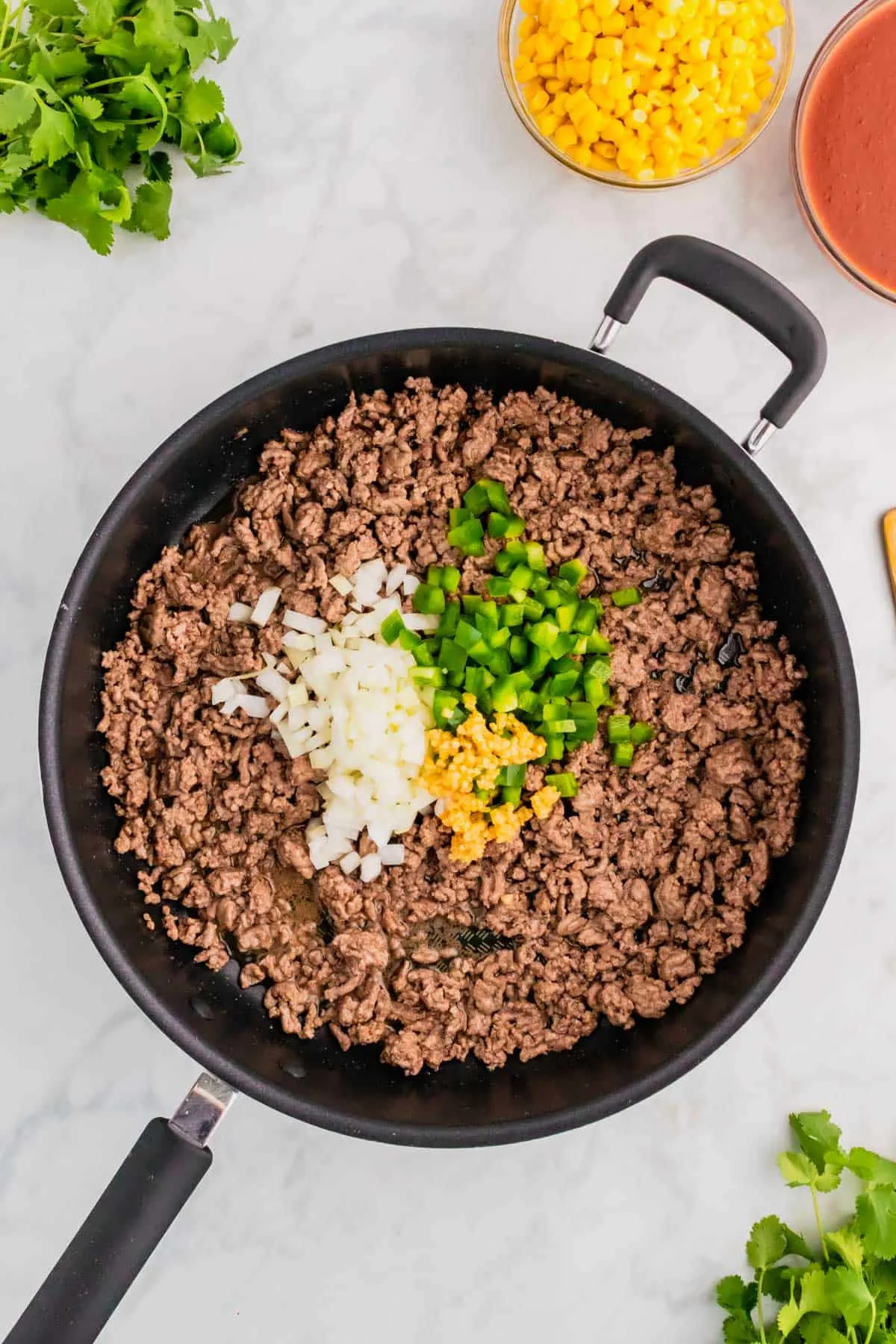 diced onions, diced green peppers and minced garlic on top of cooked ground beef in a skillet