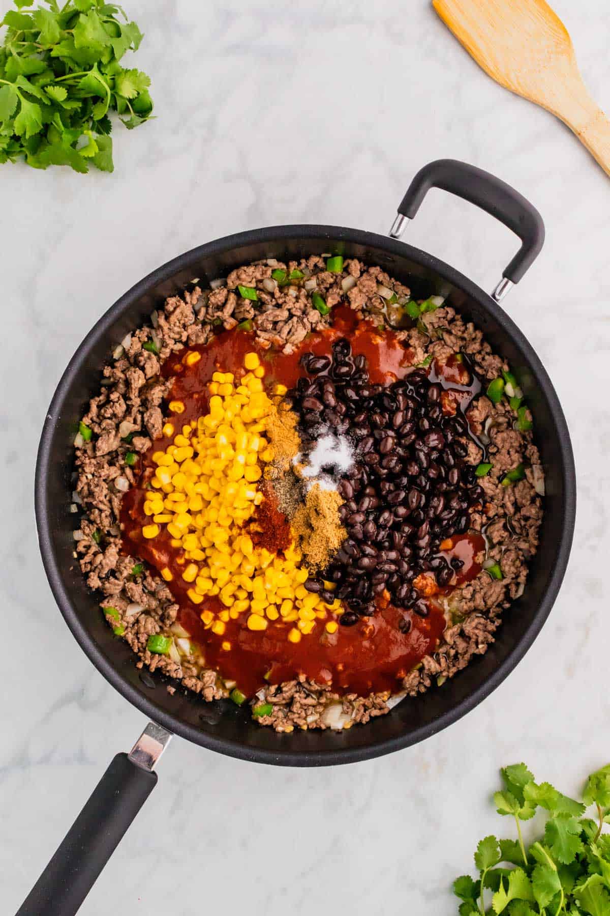 corn, black beans, spices and enchilada sauce on top of cooked ground beef in a skillet