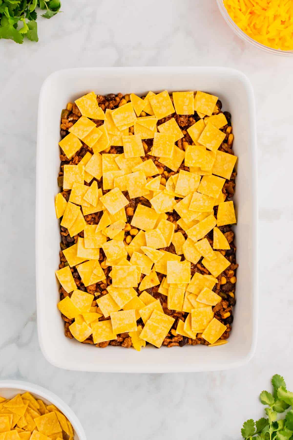 corn tortilla pieces on top of ground beef enchilada mixture in a baking dish