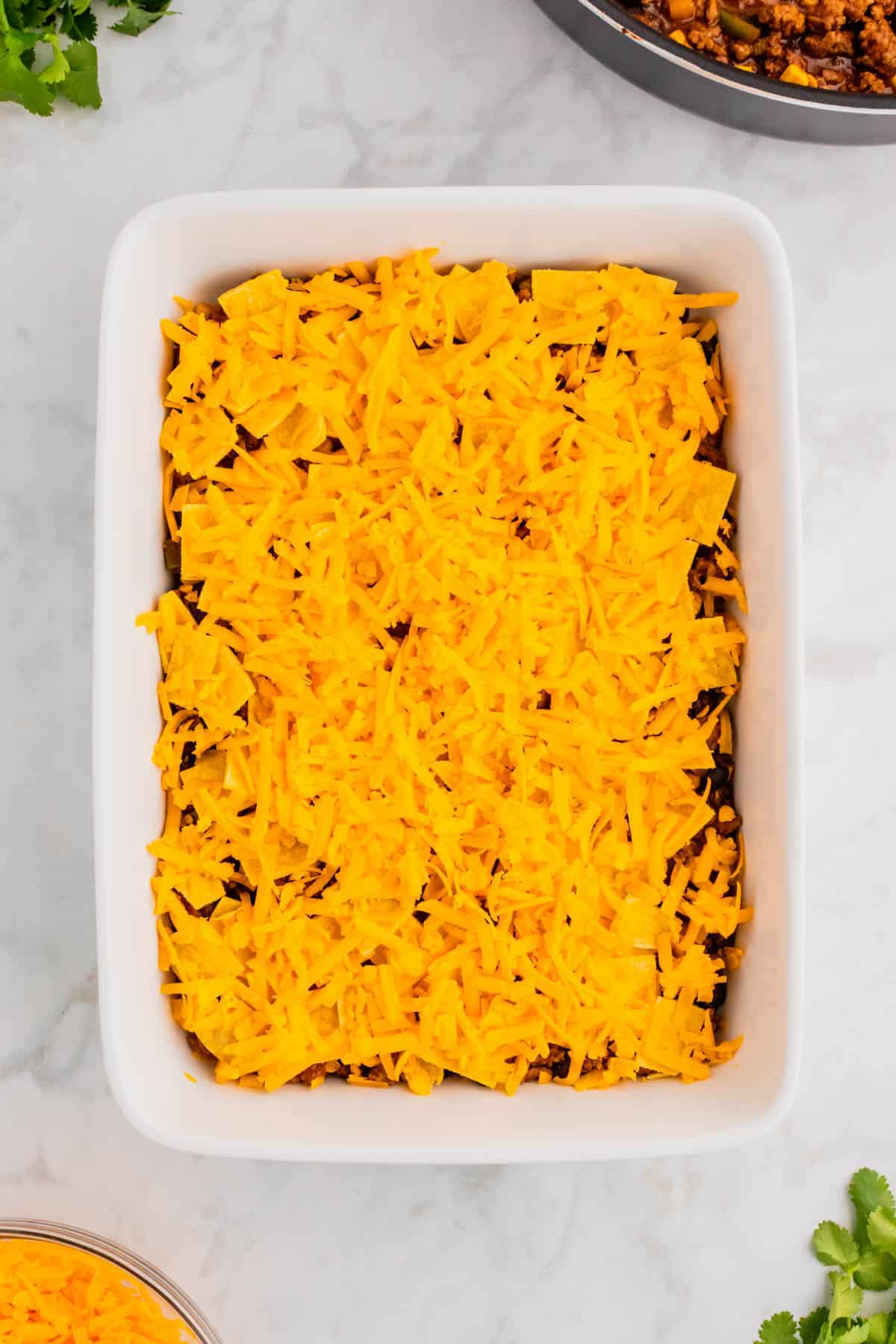 shredded cheddar cheese on top of tortillas and ground beef in a baking dish