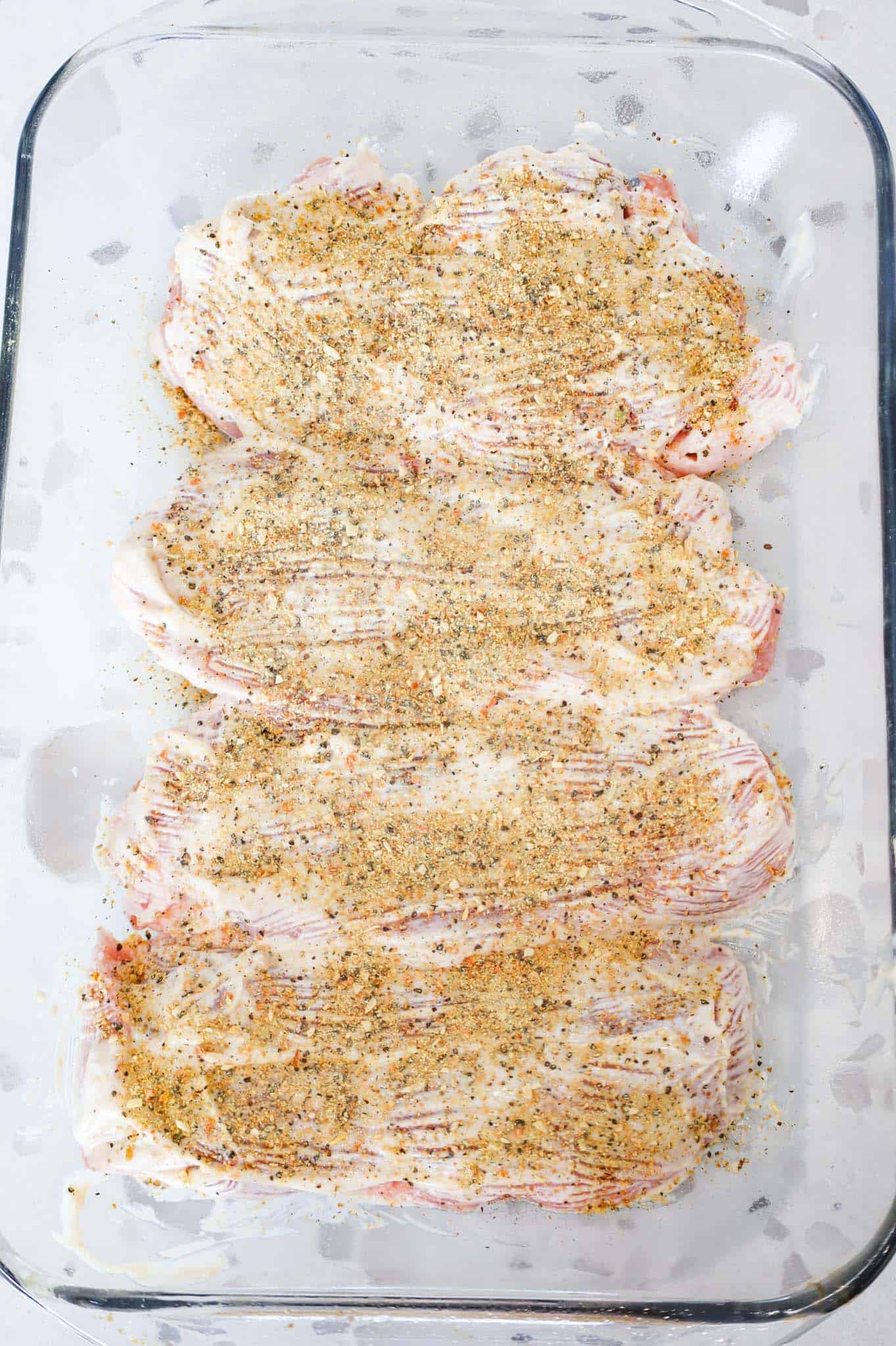 lemon pepper sprinkled on top of mayo coated pork chops in a baking dish