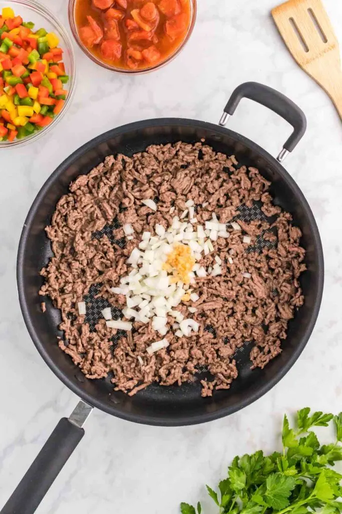 minced garlic and diced onions on top of cooked ground beef in a skillet