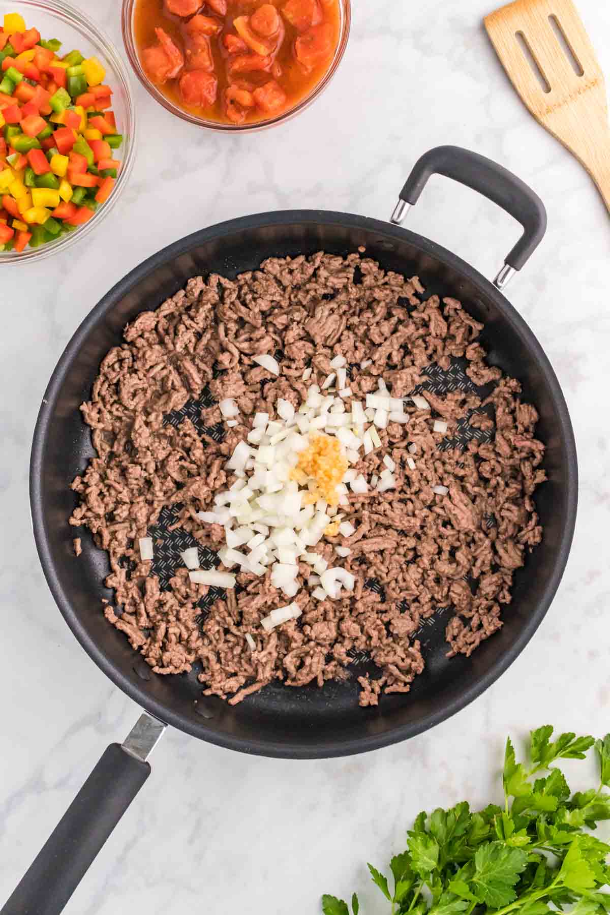 minced garlic and diced onions on top of cooked ground beef in a skillet