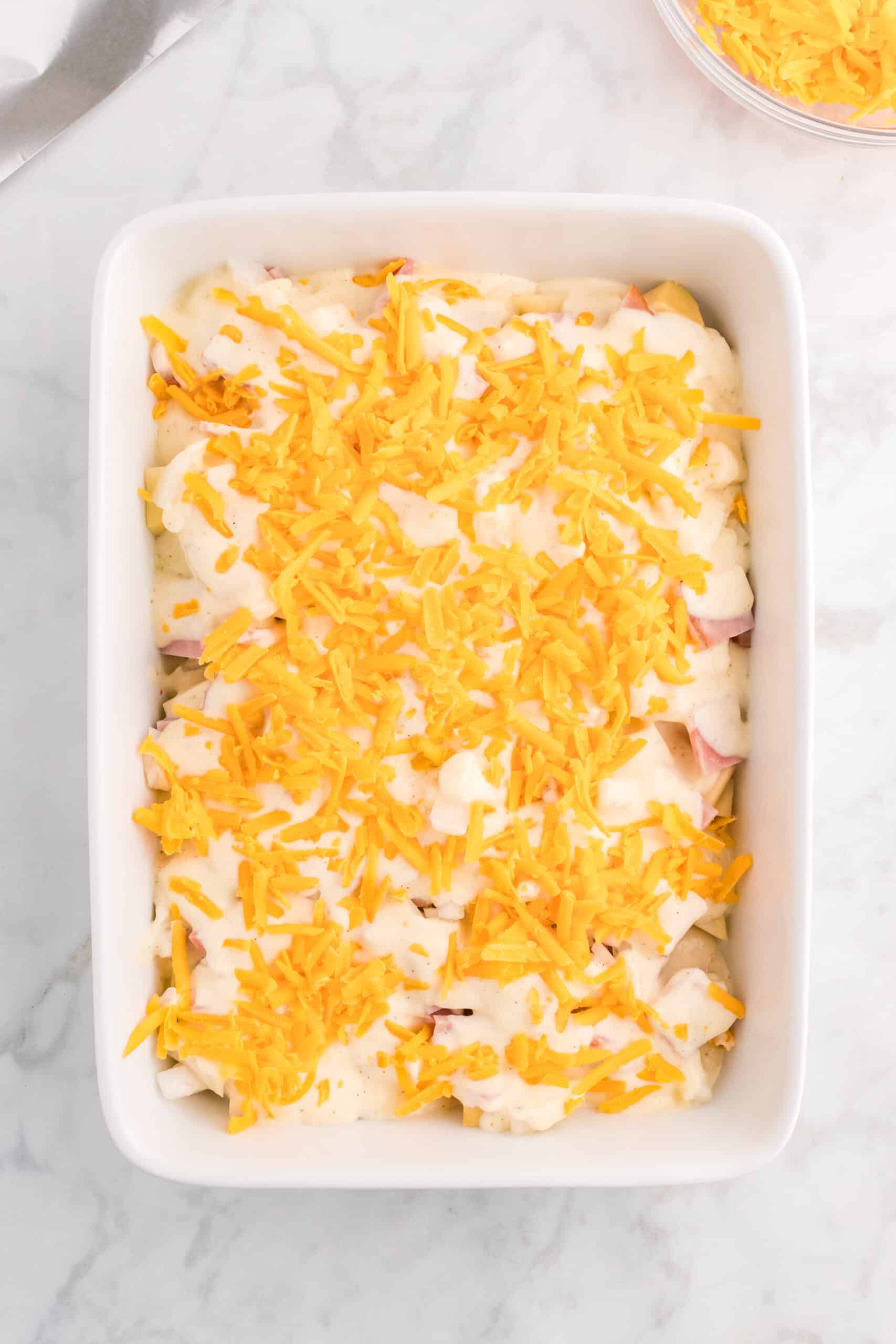 shredded cheese on top of soup mixture over ham and potatoes in a baking dish