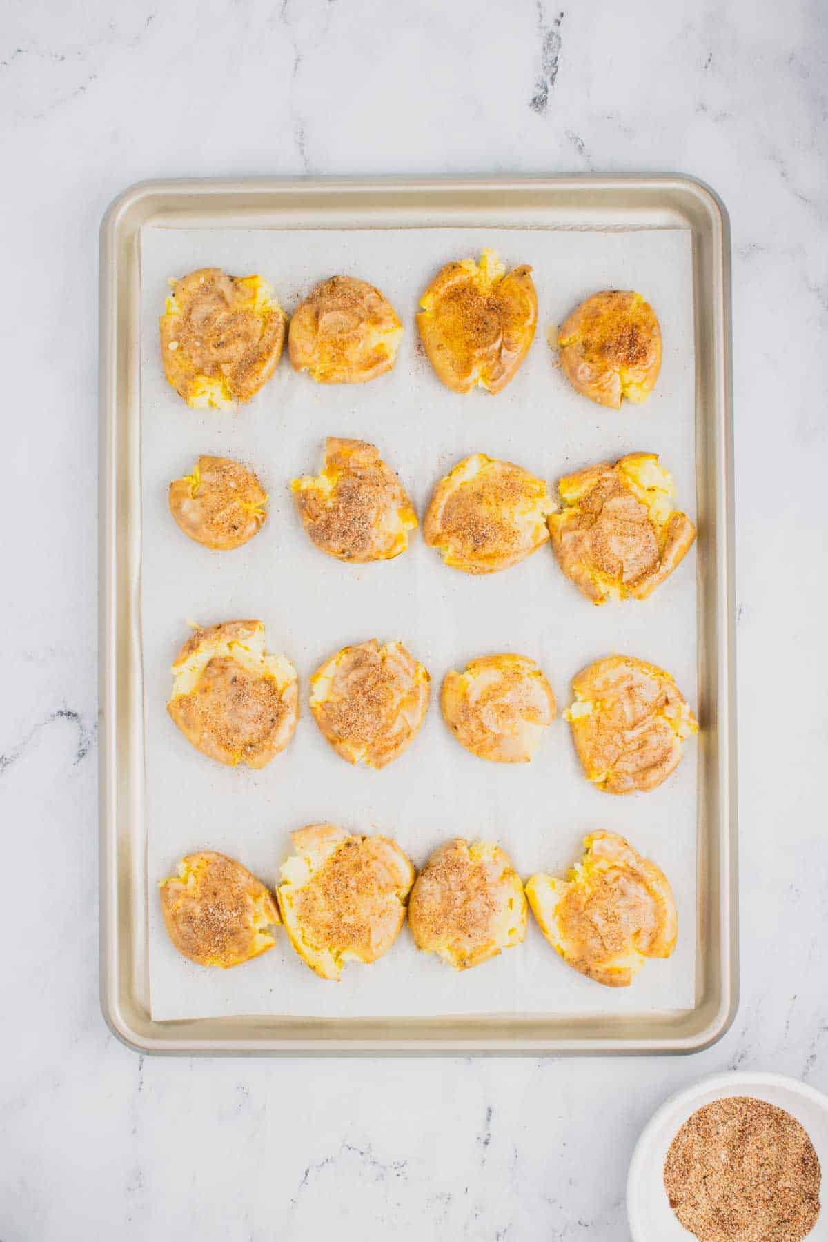 seasoning sprinkled on smashed potatoes on a baking sheet