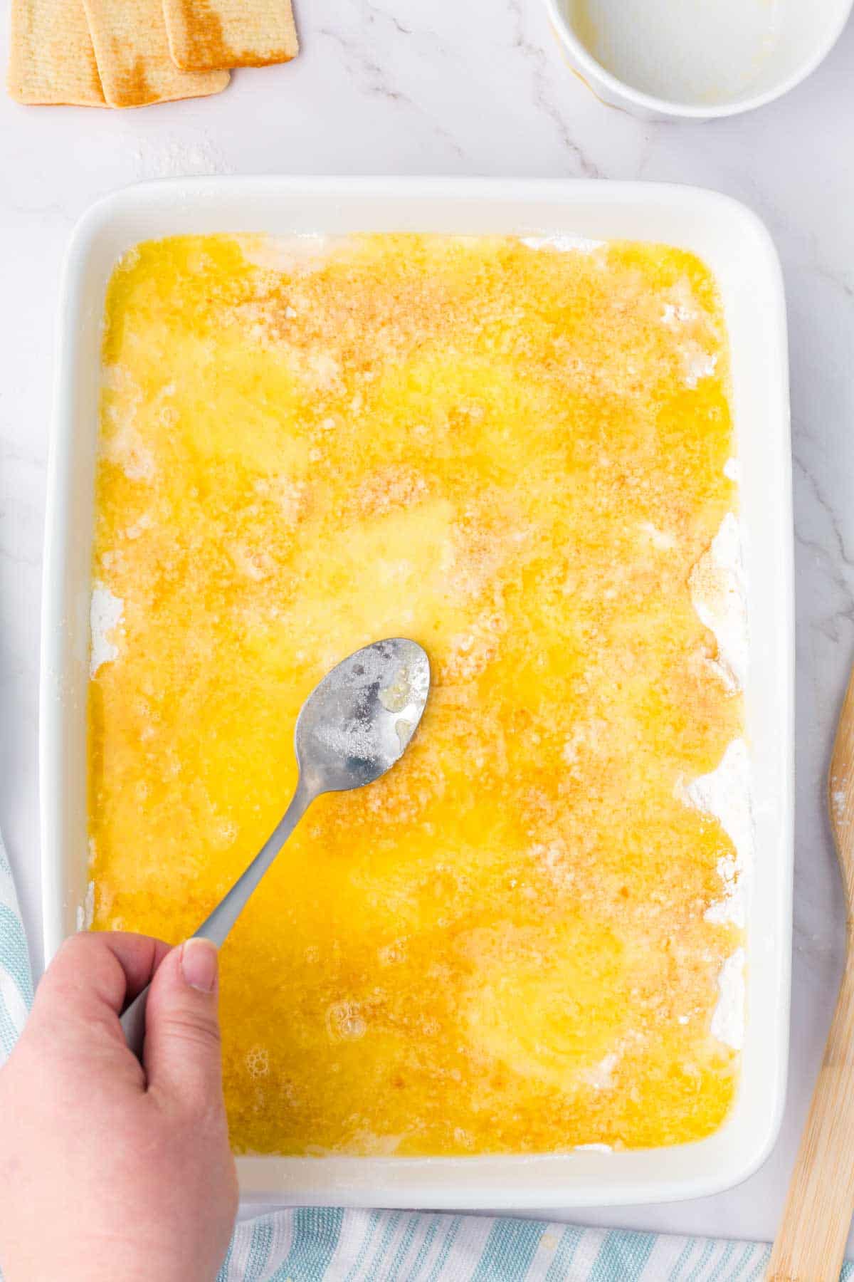 using a spoon to spread melting butter over cake mix in a baking dih