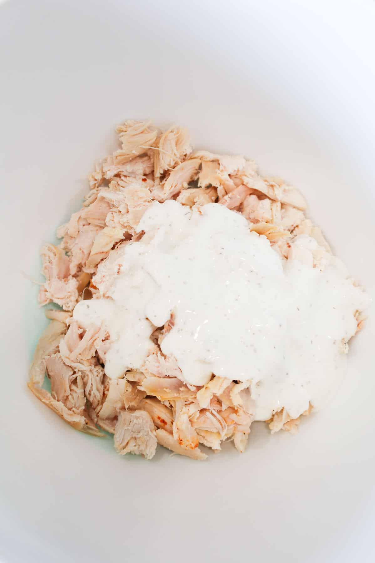 ranch dressing on top of shredded chicken in a mixing bowl