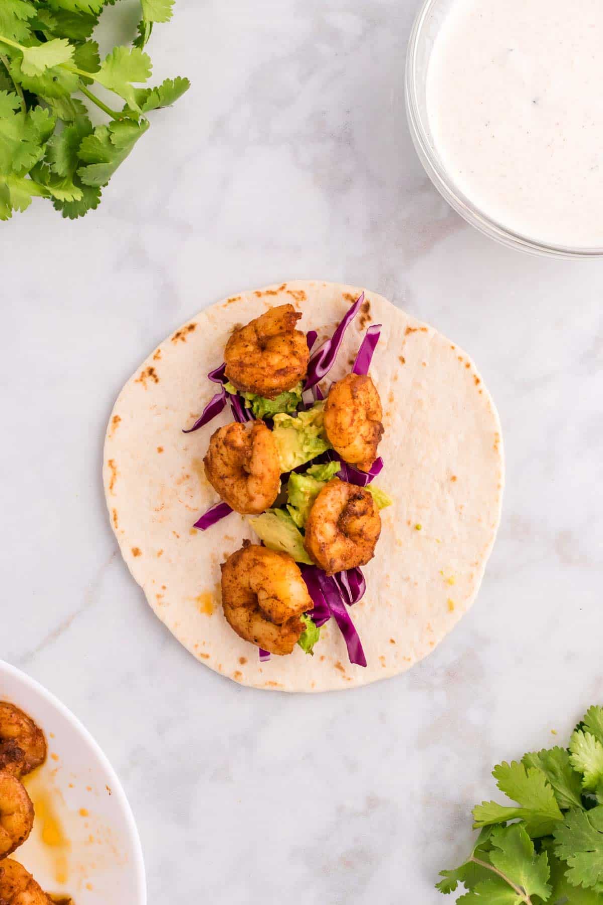 seasoned cooked shrimp on top of cabbage and avocado on a tortilla