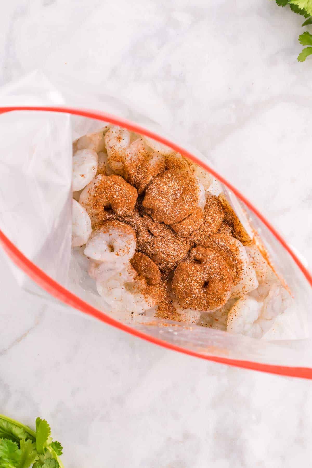 seasoning mix poured on top of raw shrimp in a large Ziploc bag