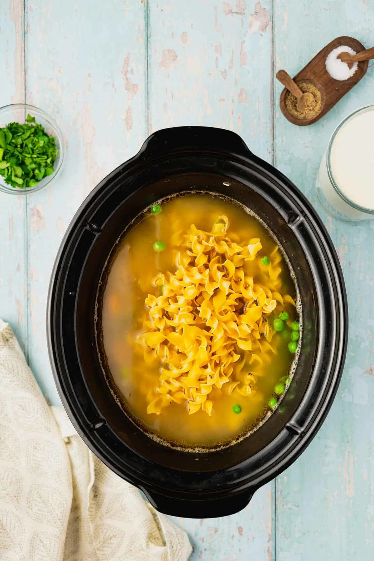 egg noodles and frozen peas added to chicken soup in a slow cooker