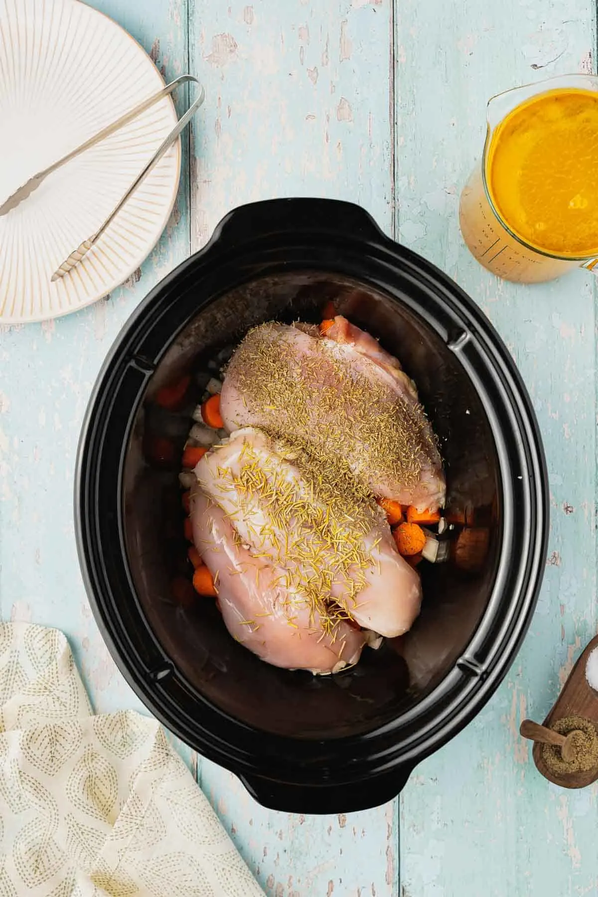 seasoned chicken breasts on top of carrots and onions in a crock pot