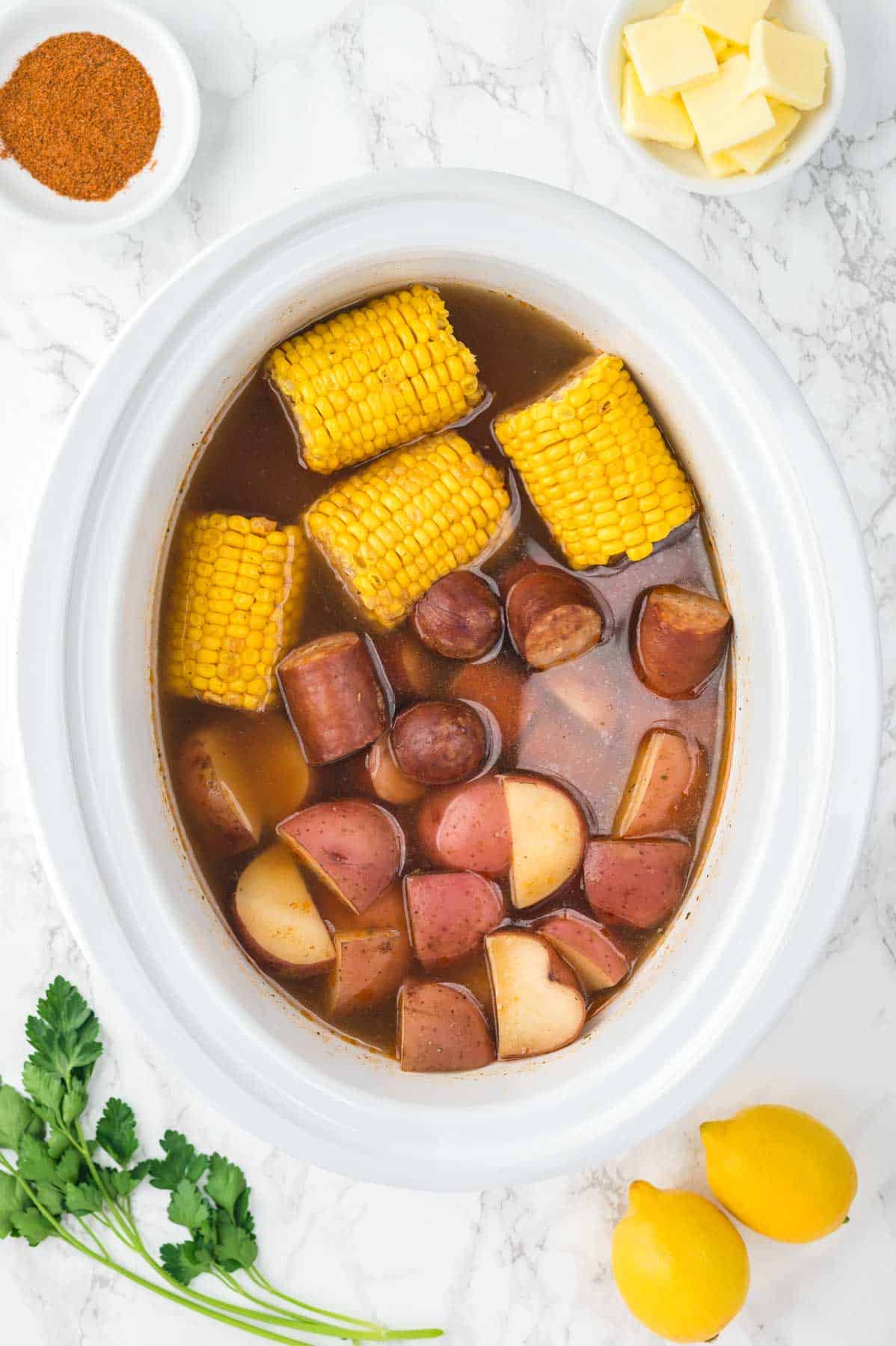 corn, sausage and potatoes cooking liquid in a slow cooker