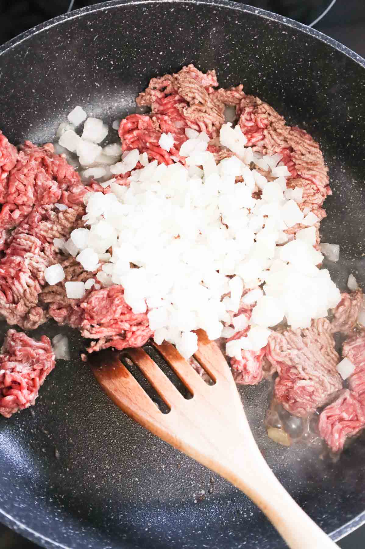 diced onions on top of ground beef cooking in a skillet