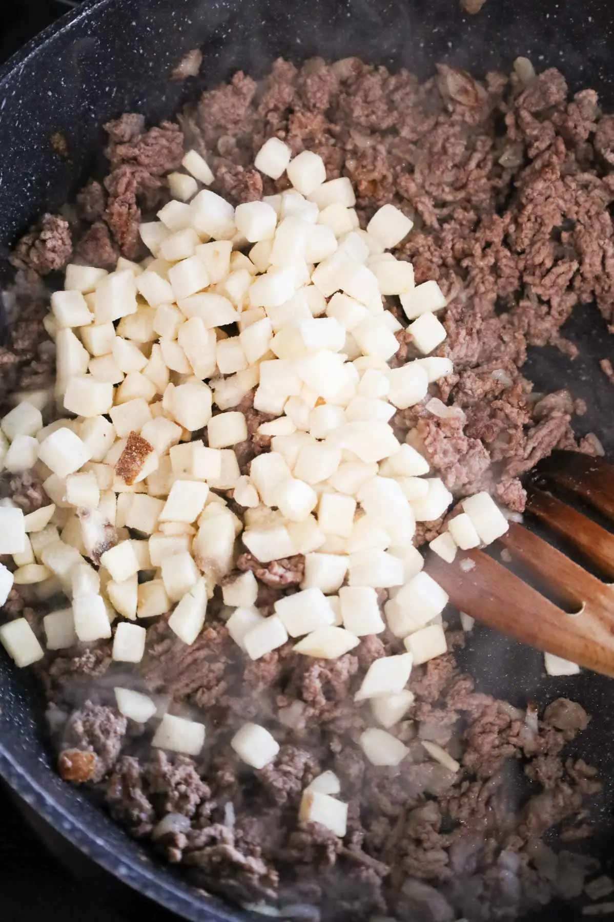 frozen diced hash brown potatoes on top of cooked ground beef in a skillet