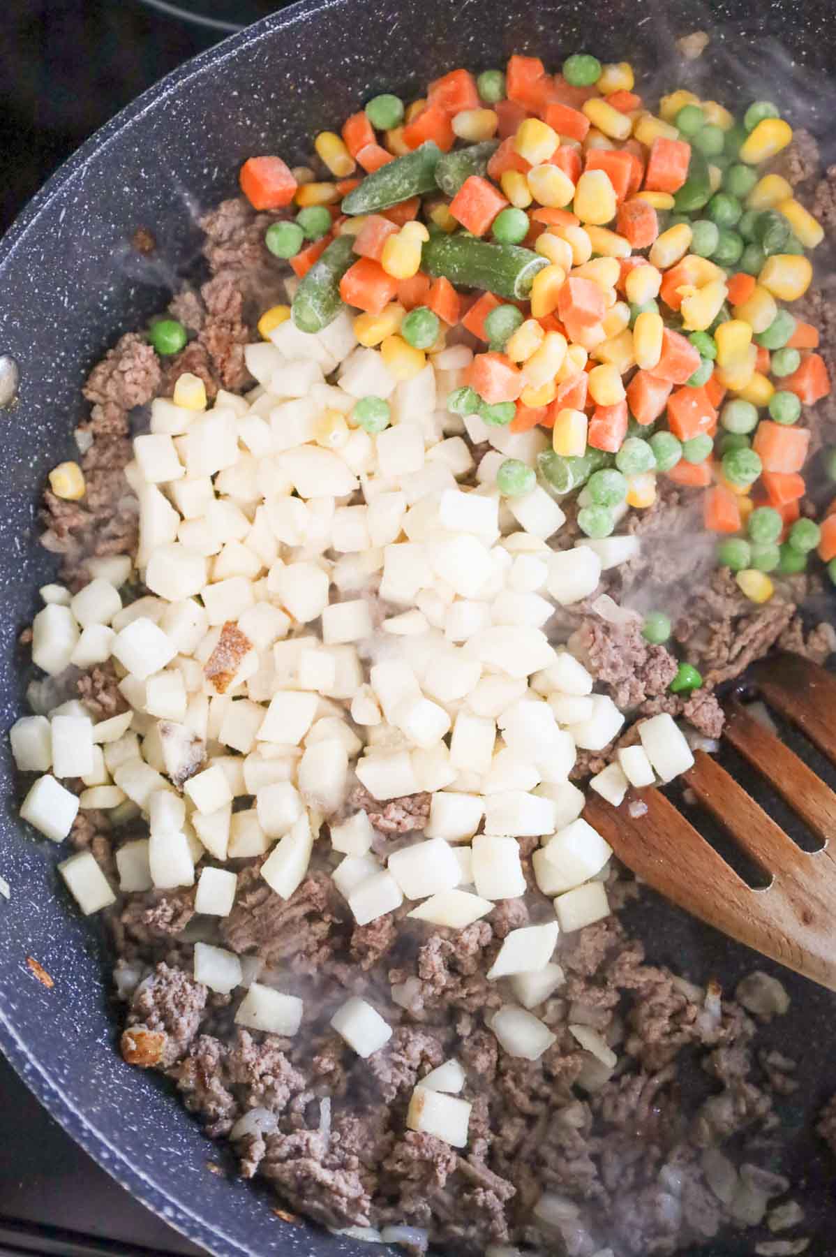frozen diced hash brown potatoes and mixed veggies on top of cooked ground beef in a skillet