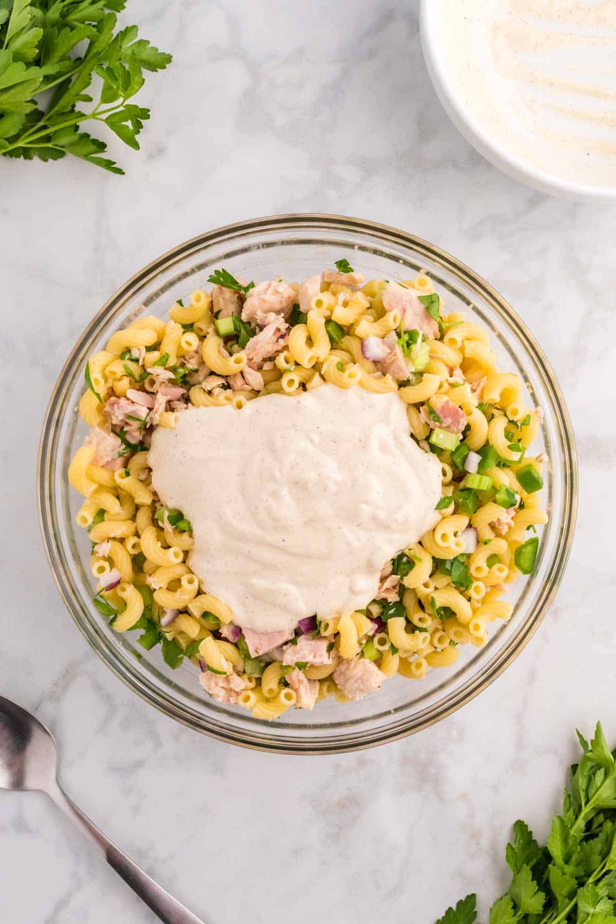 mayo dressing on top of tuna pasta salad ingredients in a mixing bowl