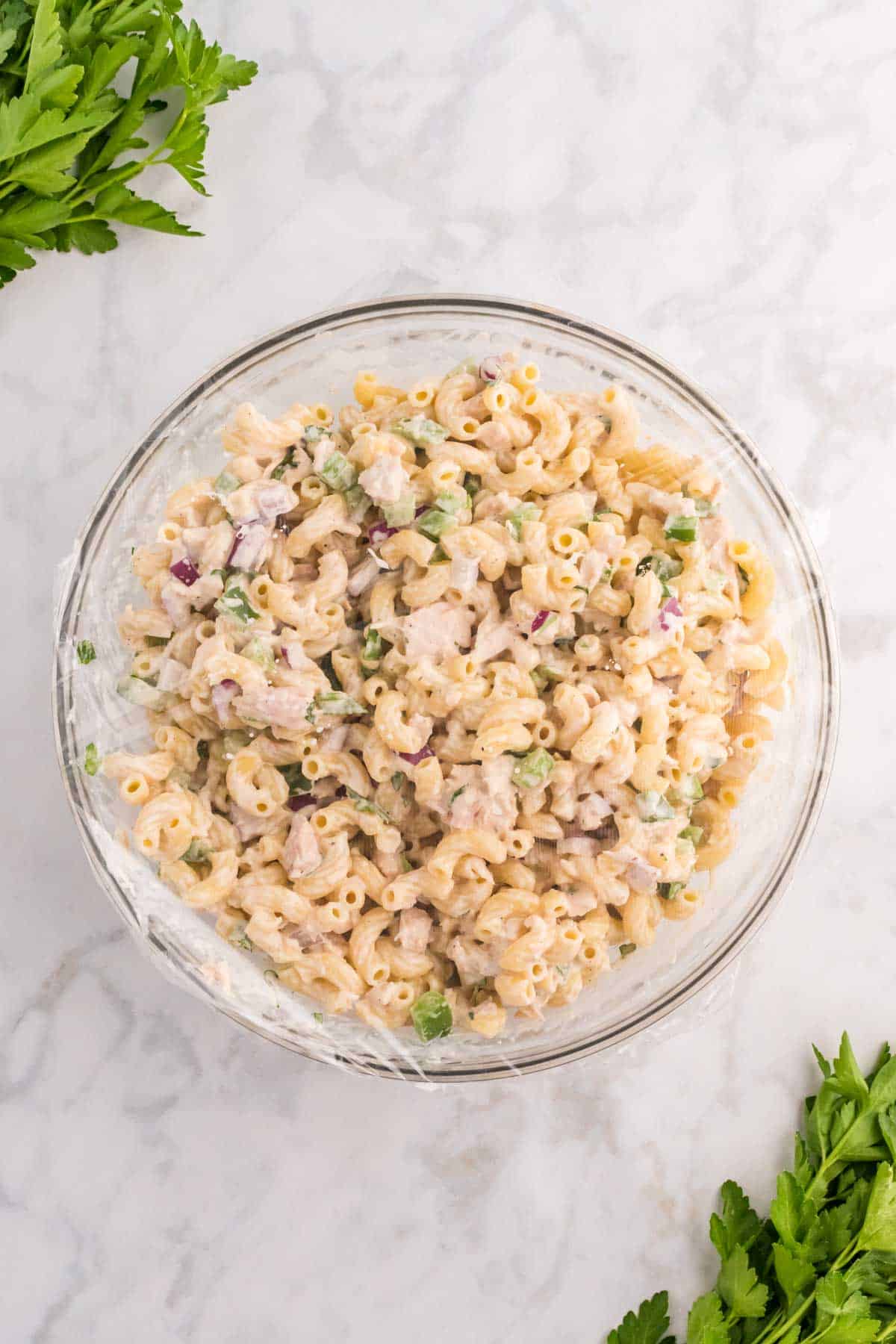 macaroni salad in a bowl covered with plastic wrap