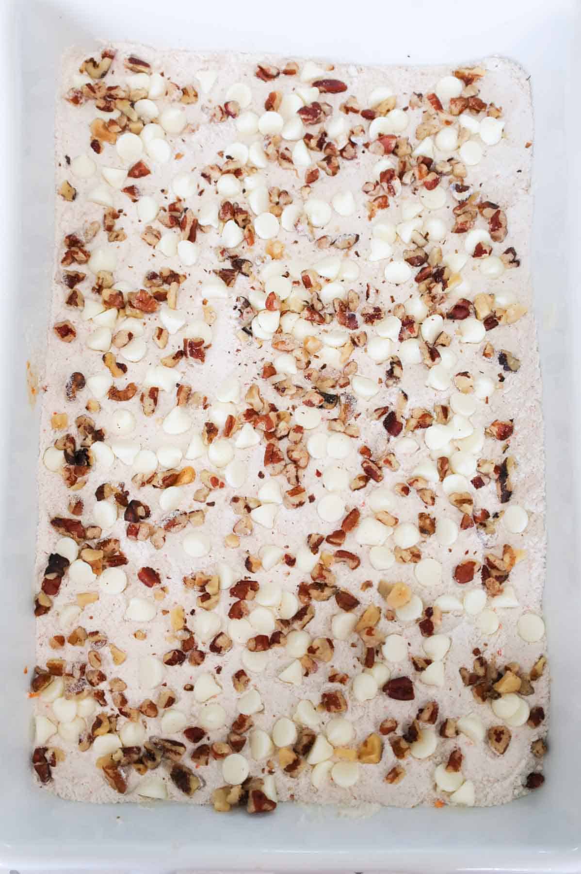 chopped pecans and cream cheese flavoured baking bits on top of dry carrot cake mix in a baking dish