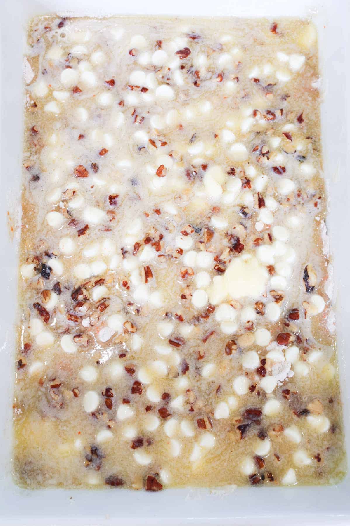 melted butter poured over cream cheese baking bits, pecans and carrot cake mix in a baking dish