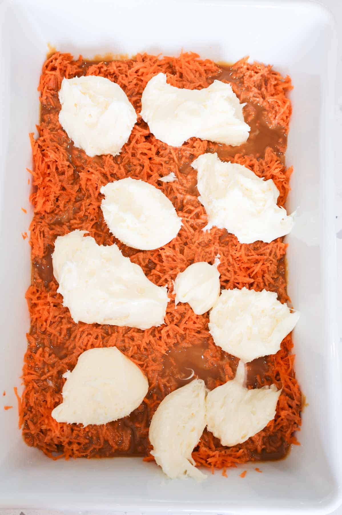 blobs of cream cheese frosting on top of dulce de leche and grated carrot in a baking dish