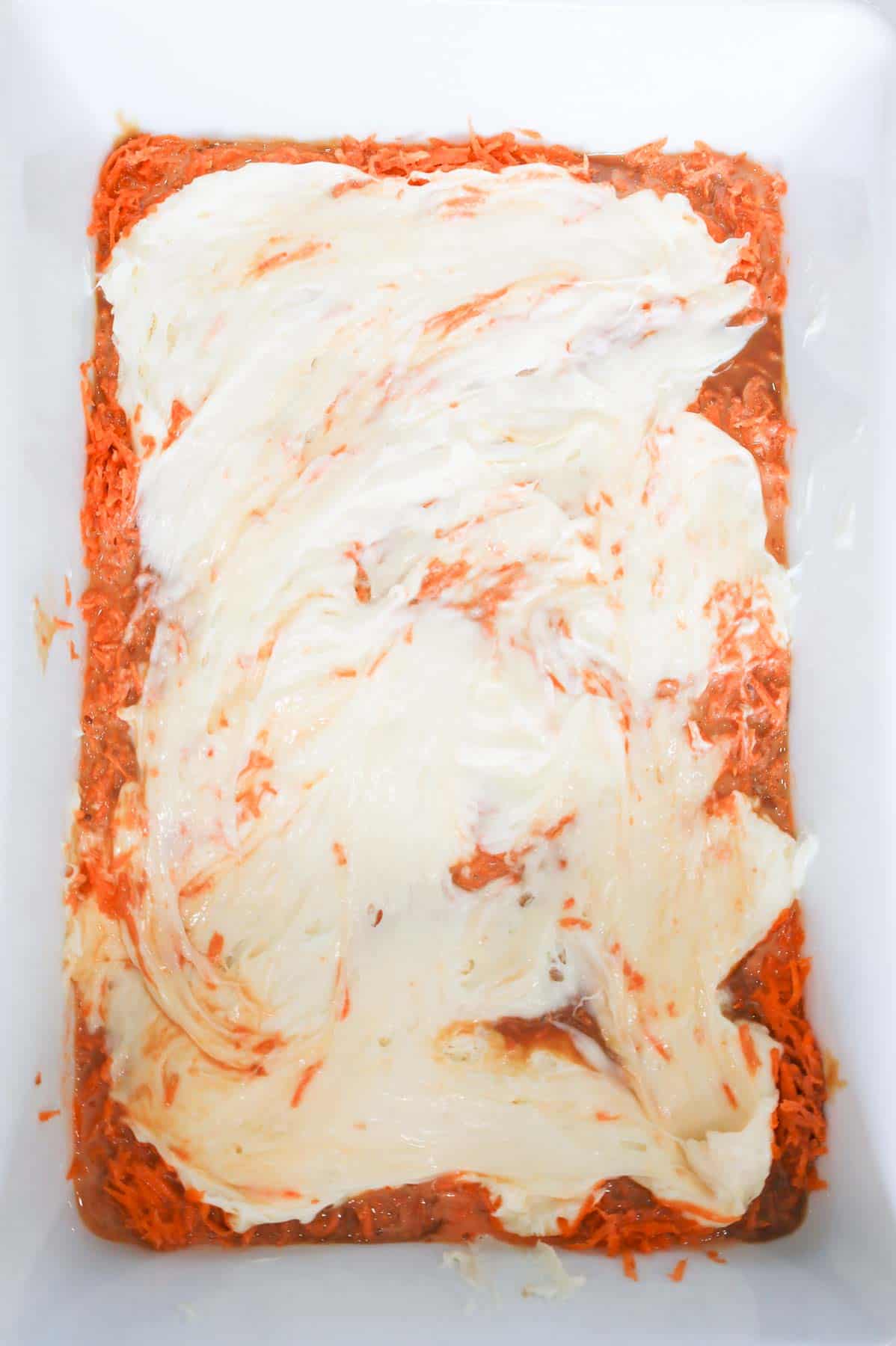 cream cheese frosting spread over grated carrot in a baking dish