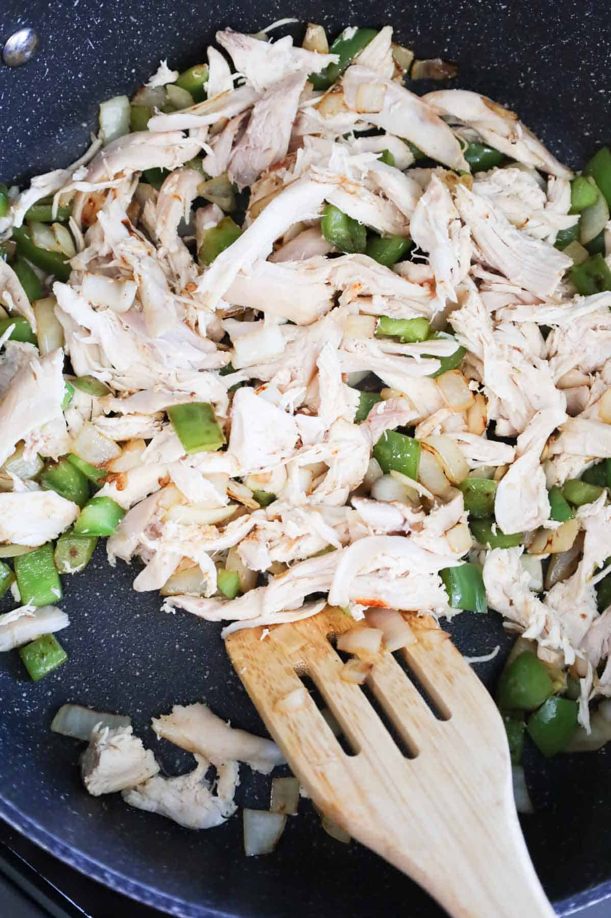 shredded chicken, diced bell peppers and diced onions being stirred in a skillet