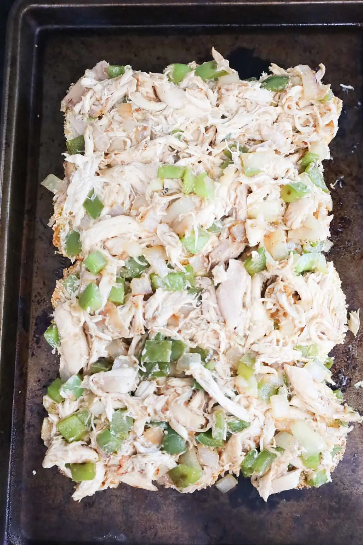 shredded chicken and bell peppers mixture on top of buns on a baking sheet.