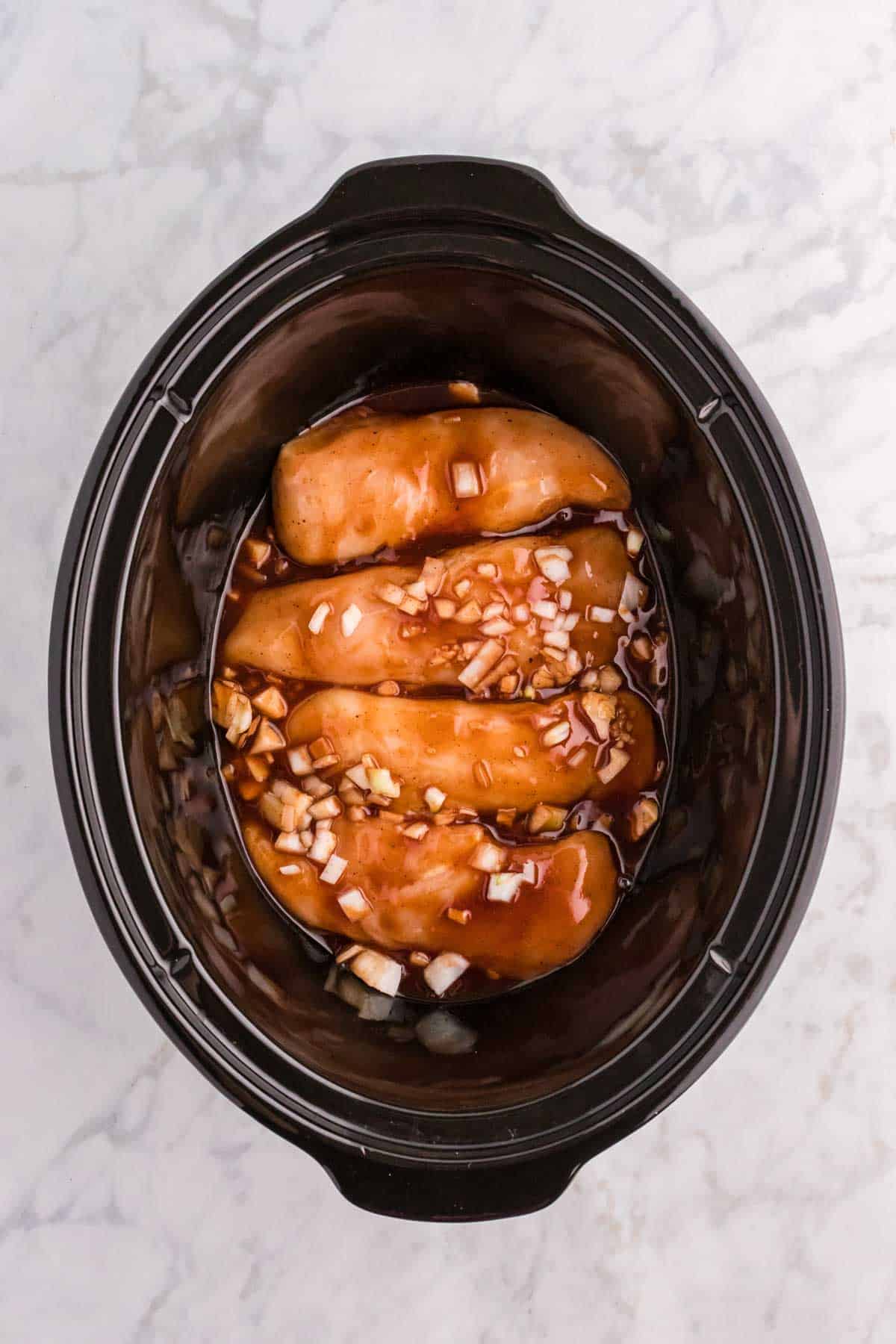 minced garlic, onions and bbq sauce on top of chicken breasts in a crock pot