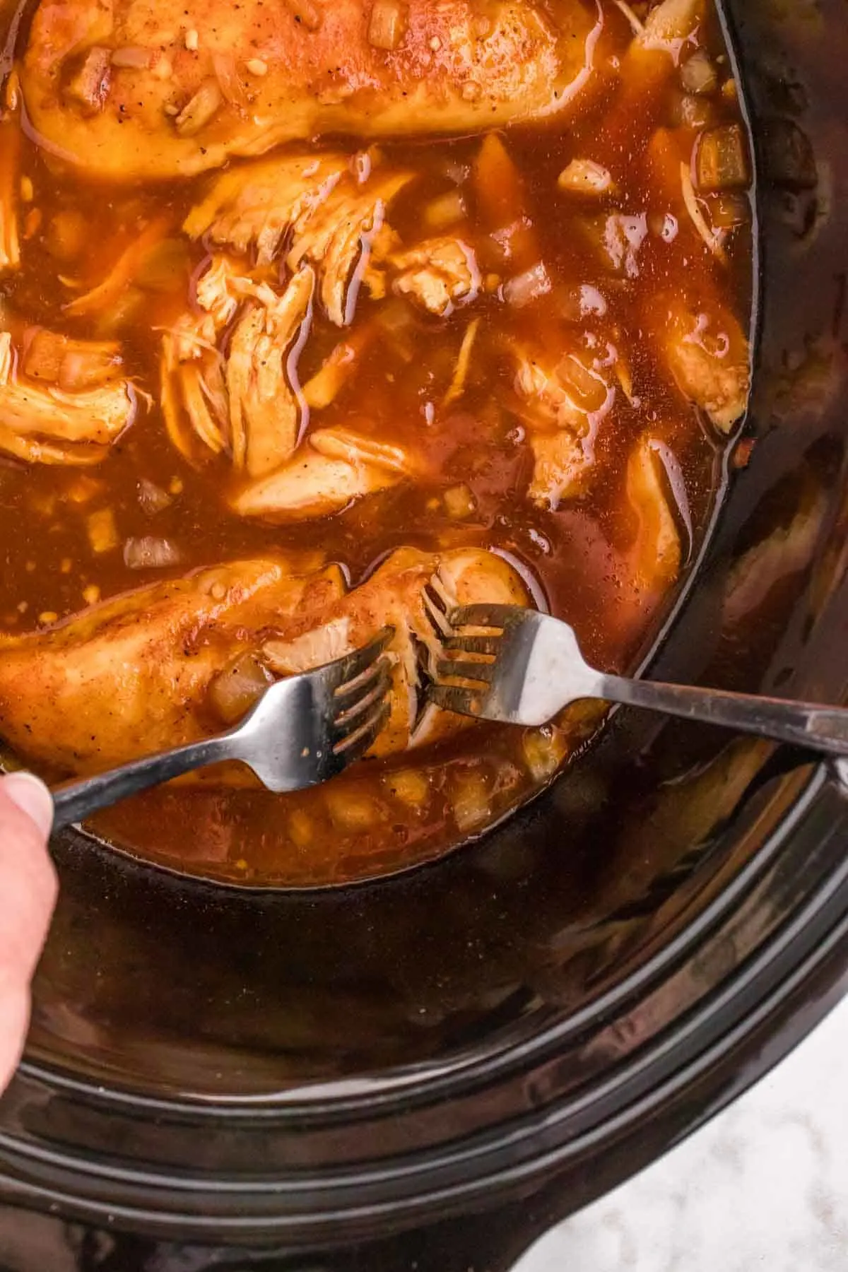 BBQ chicken in a Crock Pot being shredded with two forks