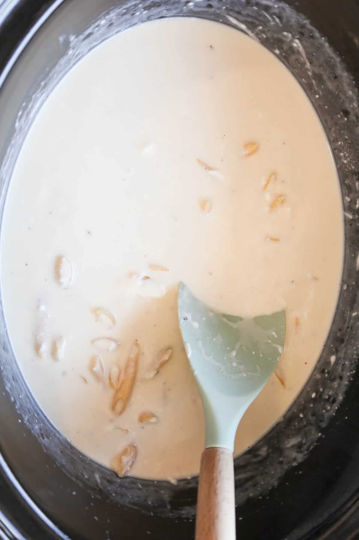 stirring penne noodles into garlic parmesan sauce mixture in a crock pot