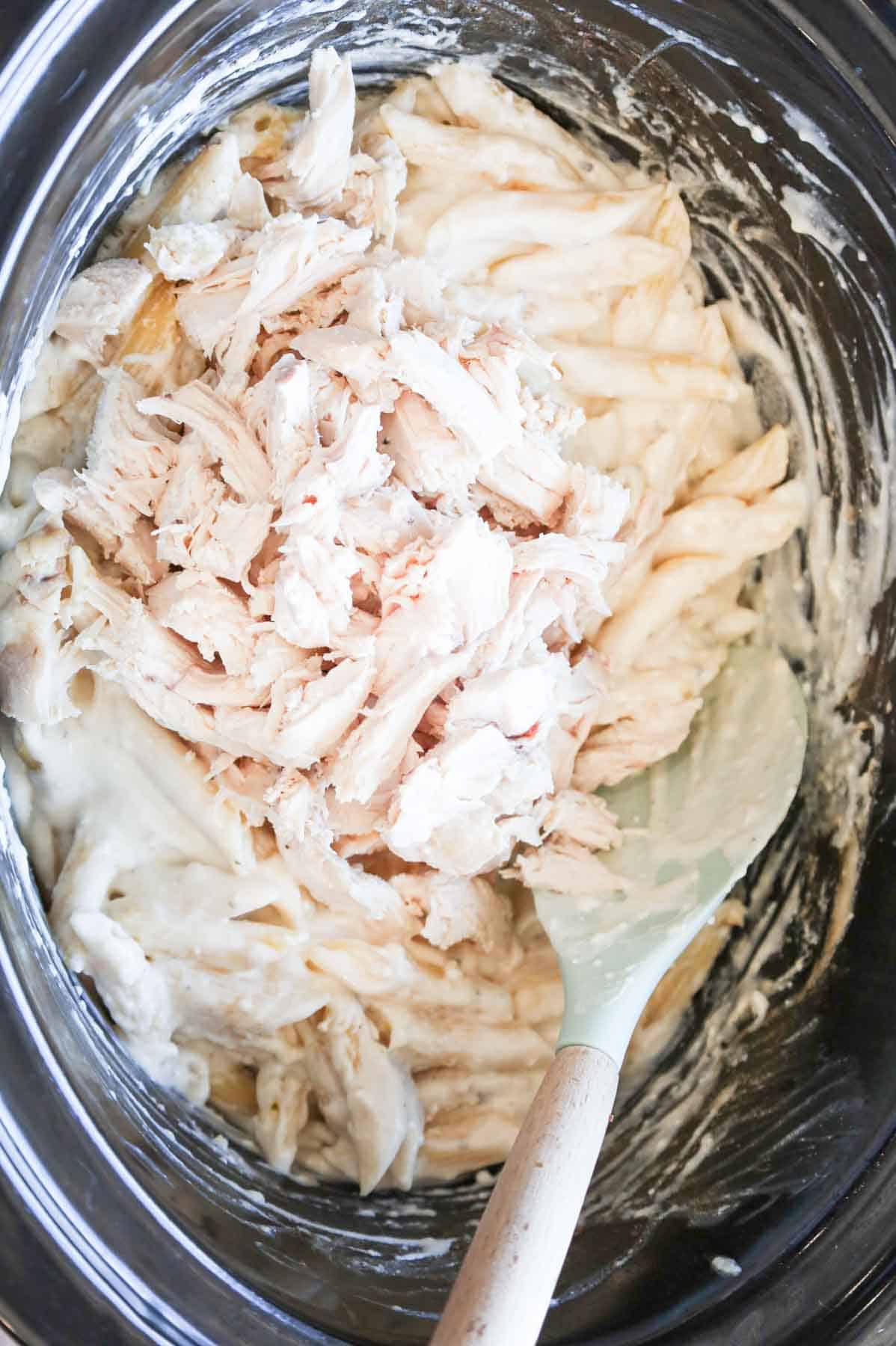 shredded chicken on top of creamy chicken pasta in a crock pot